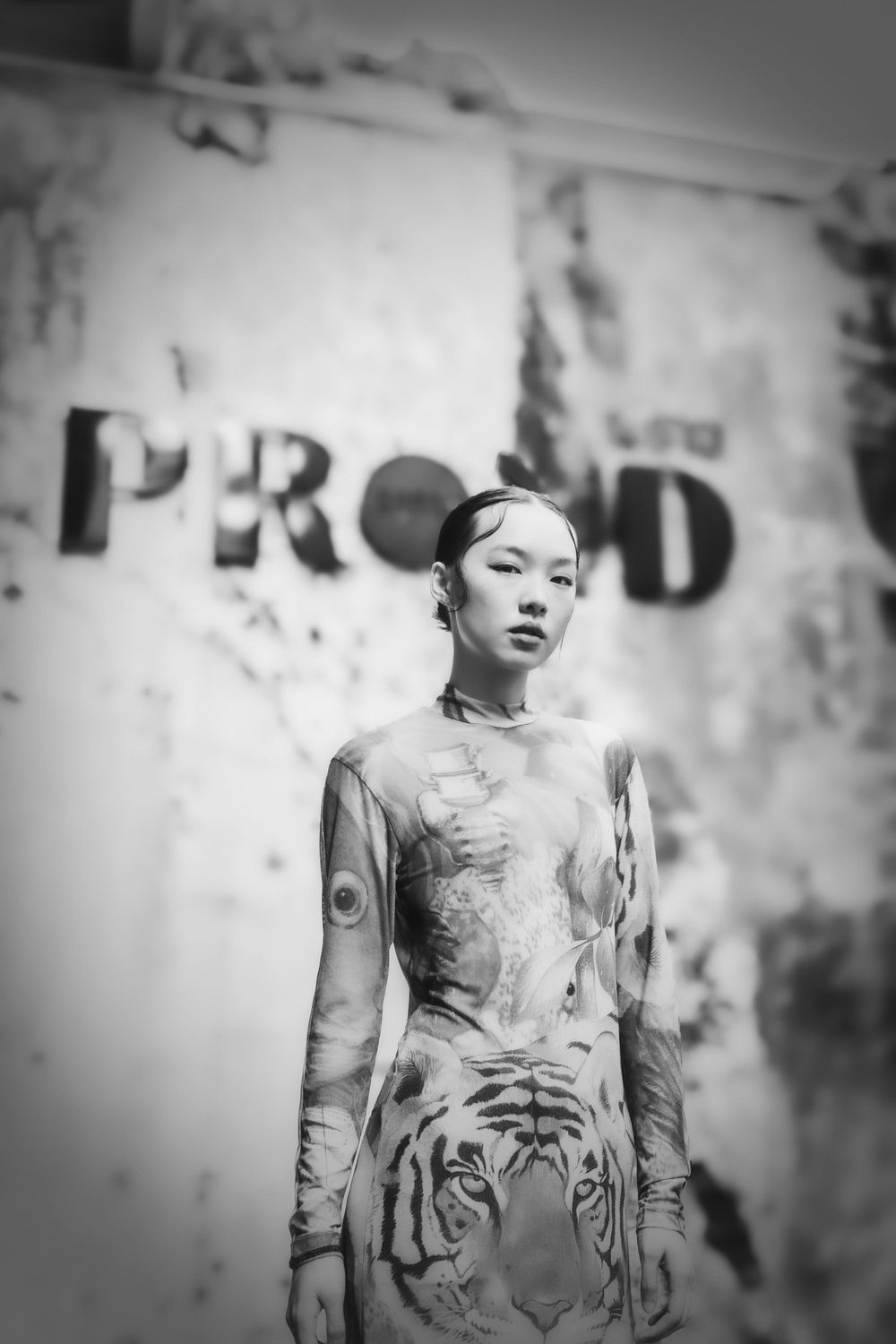 Black and white fashion photograph featuring a model wearing a tiger print dress against a textured wall with PROUD text.