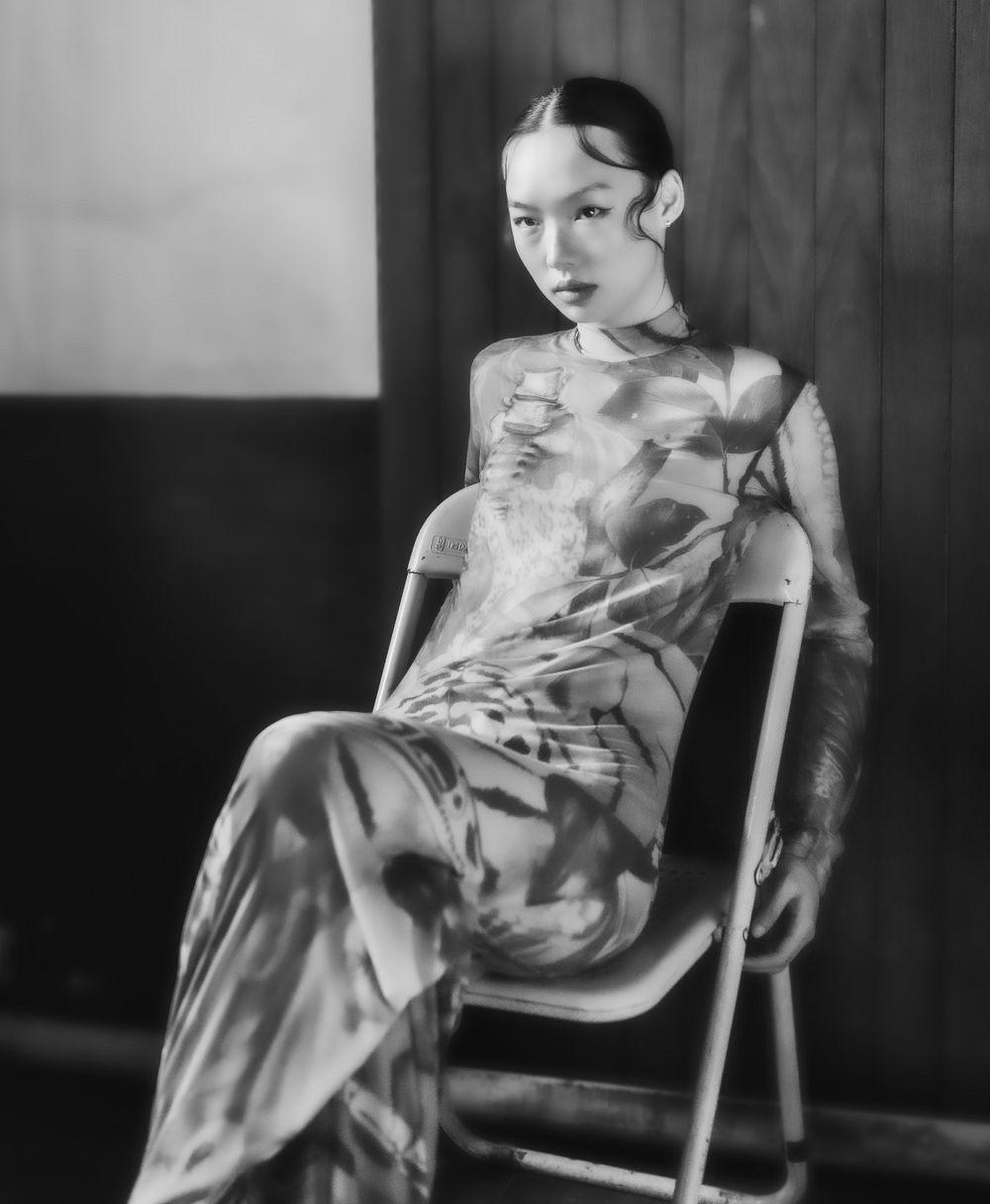 A vintage black and white photo shows someone seated in traditional Chinese dress with a qipao gown and styled hair.
