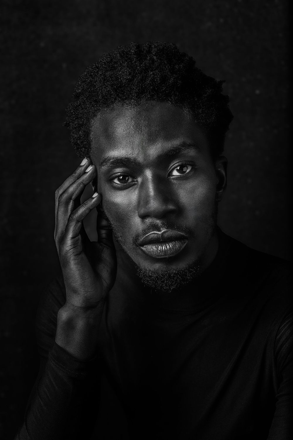 Dramatic black and white portrait showing intense gaze and contemplative pose against dark background.