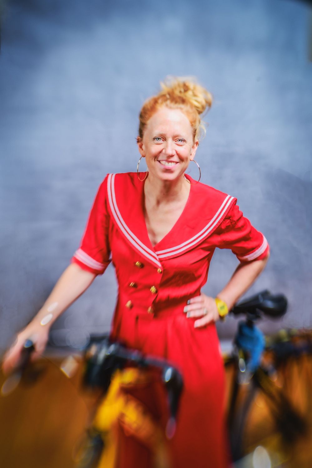 An individual wearing a bright red dress with white trim stands beside bicycles in an outdoor setting.