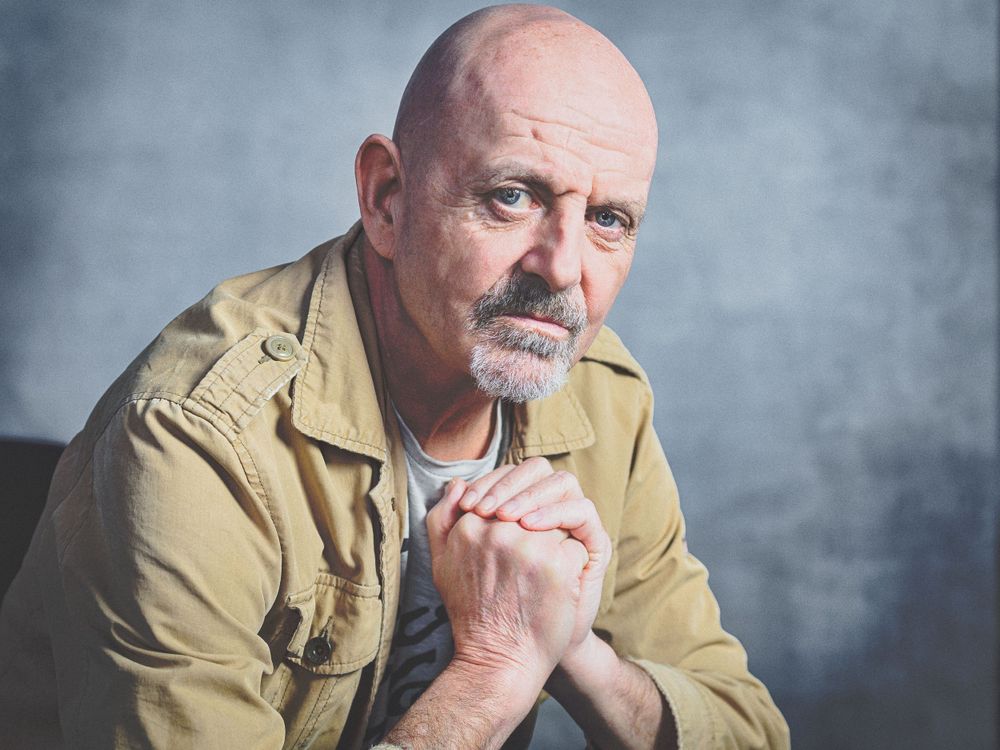 Portrait of a contemplative man in tan jacket against grey background.