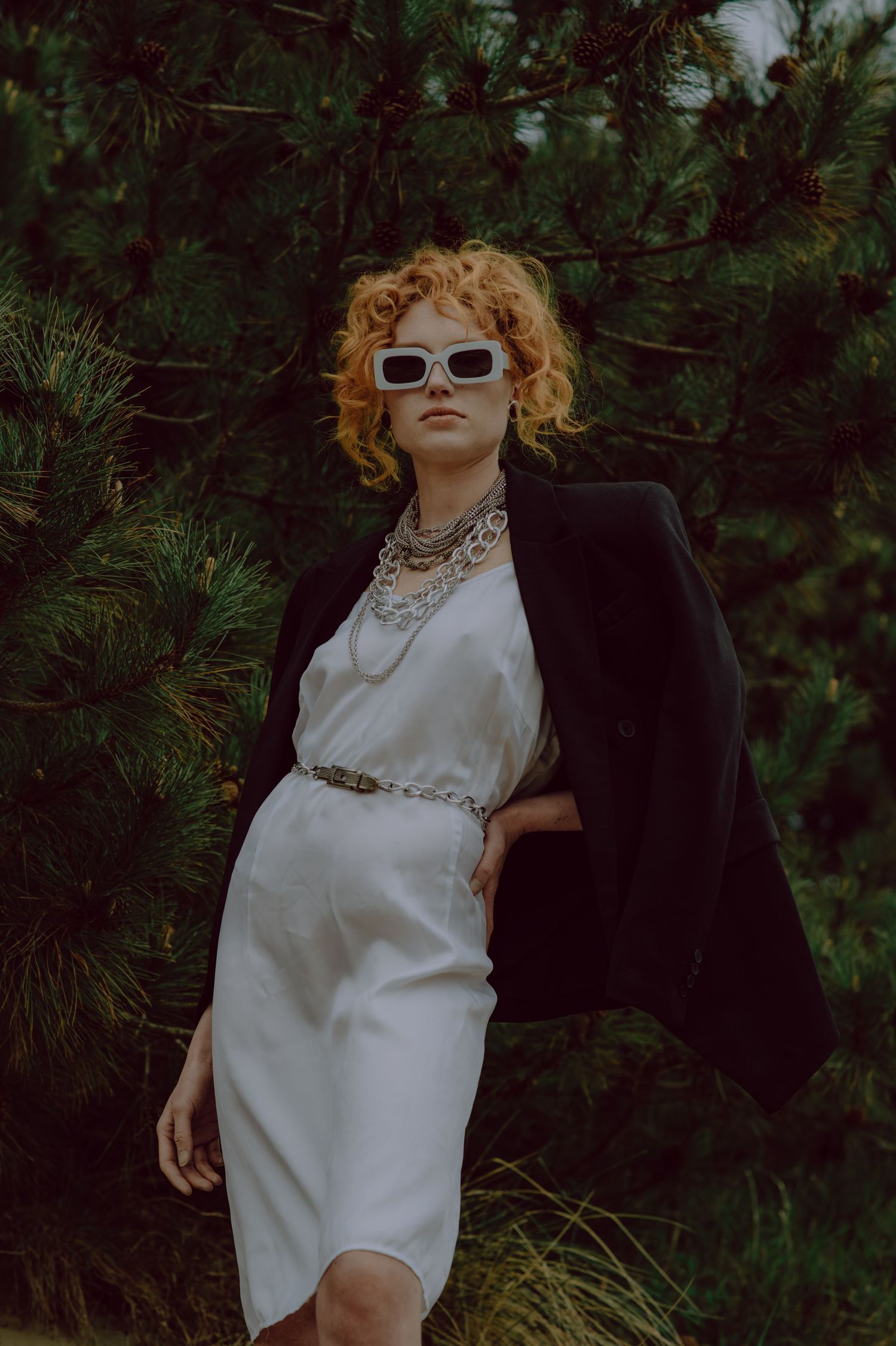Artistic portrait showing a bare back with curly red hair and delicate necklace against moody lighting.