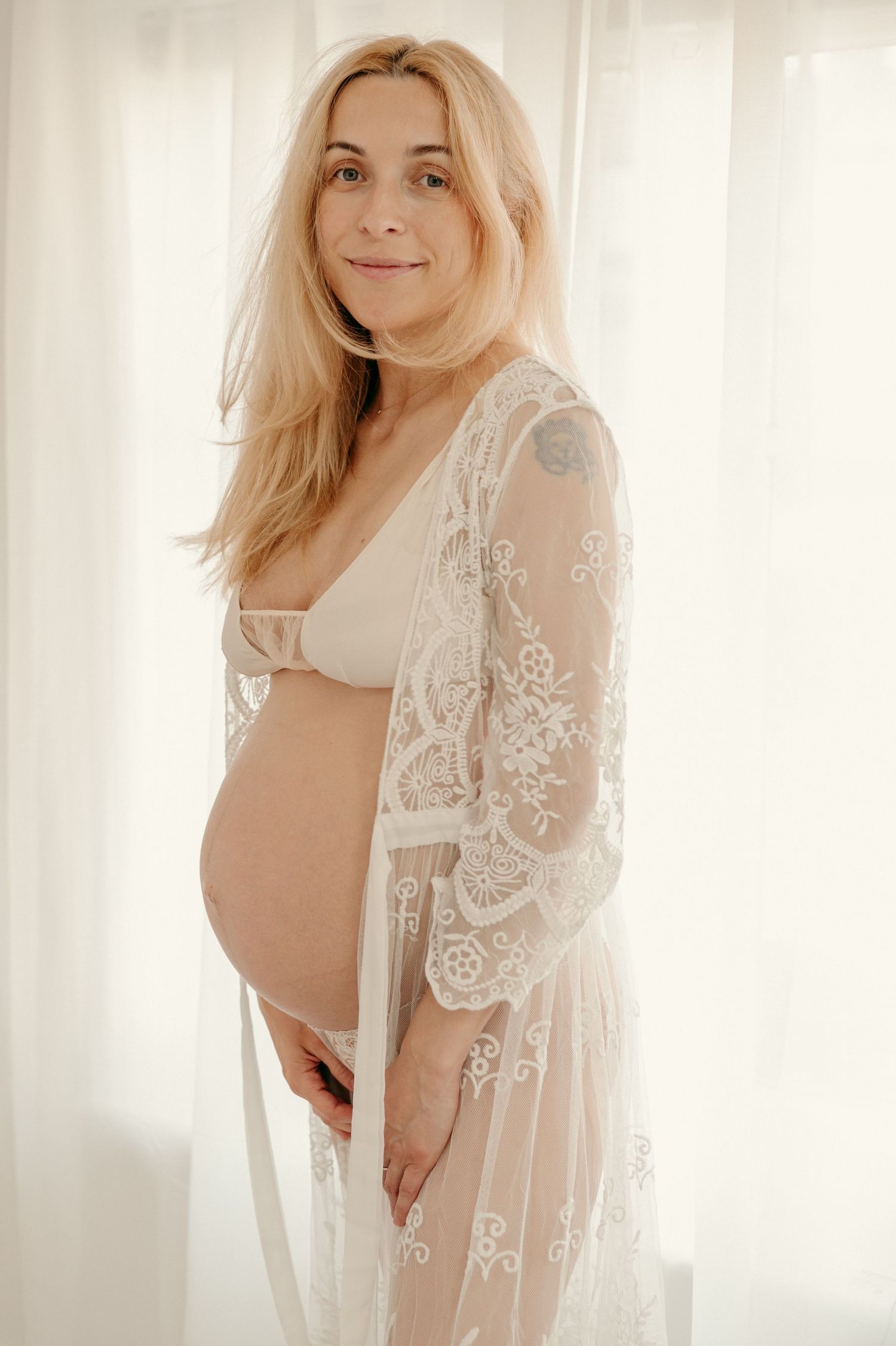 Dreamy maternity session with lace details and soft window light creating an ethereal atmosphere.