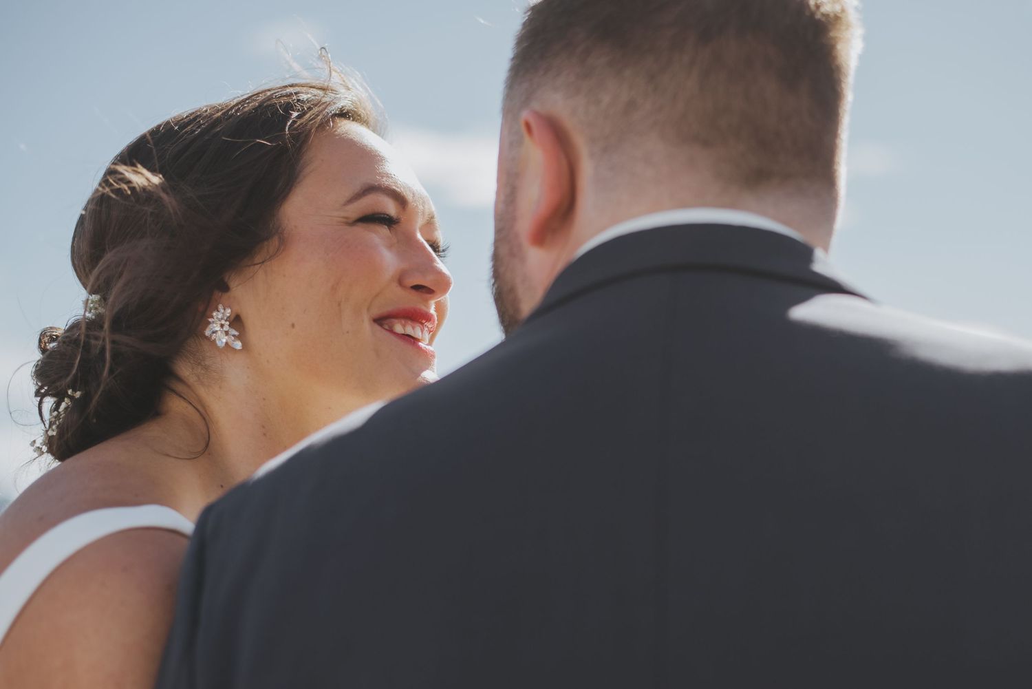 Close up profile view of a bride in white dress with tiara smiling during outdoor wedding ceremony.