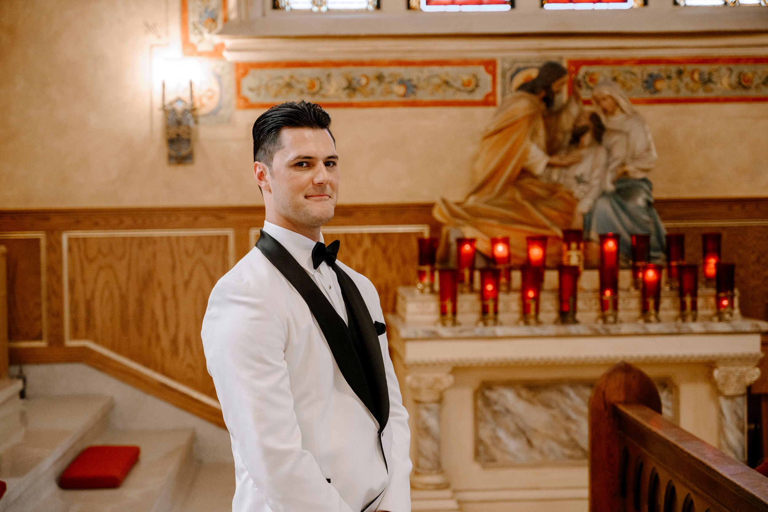Server wearing black vest and white shirt carries beverage tray through elegant restaurant dining room with ornate decor.