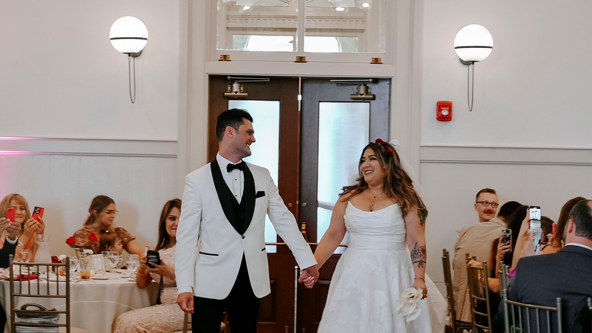 A couple shares their first dance at an elegant indoor wedding reception with guests watching from round tables.