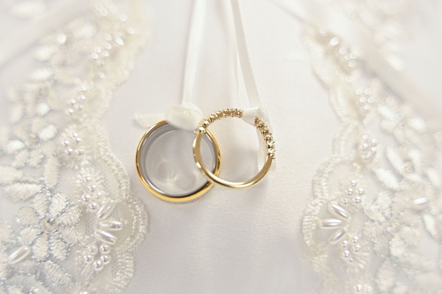 A collection of blue and white wedding rings laid out beside navy blue satin ribbons and rose petals.