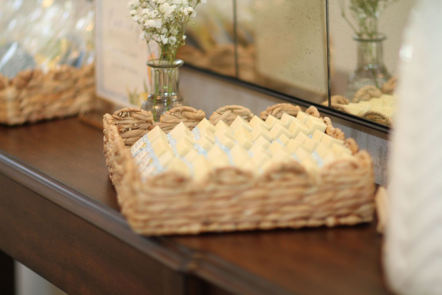 Woven wicker basket filled with folded white linens sits on dark wooden table beside small vase of flowers.