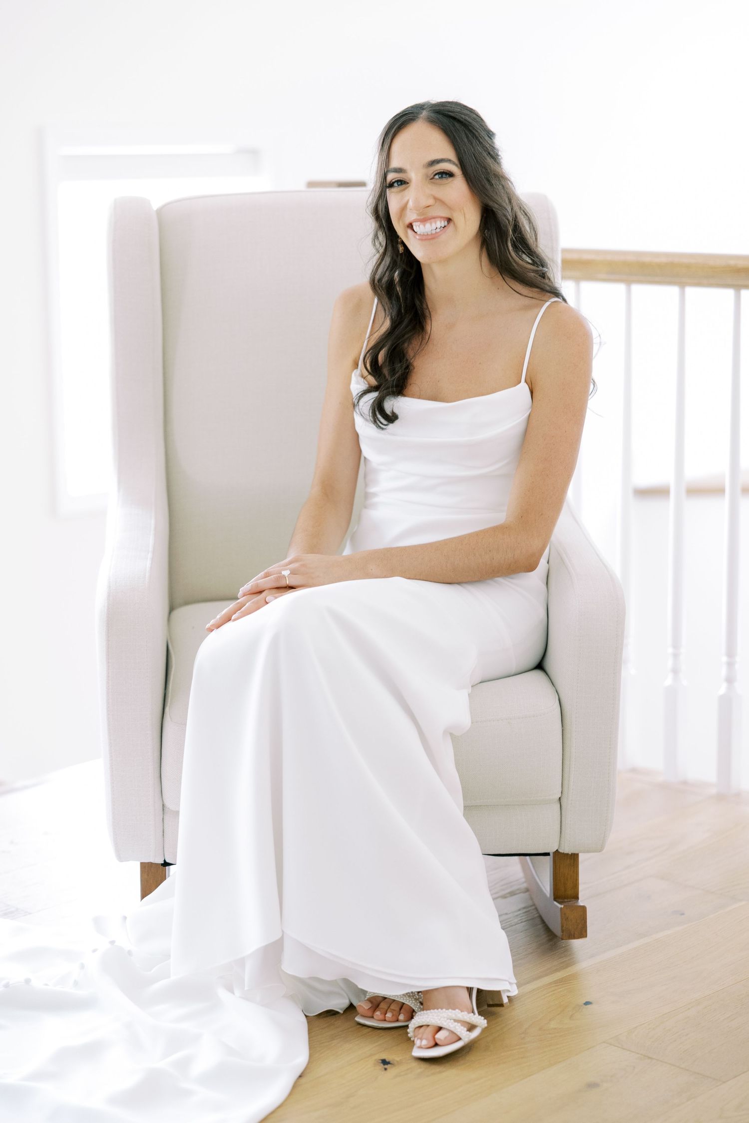 A person in a white dress relaxes on a modern white couch in a bright, minimalist interior setting.