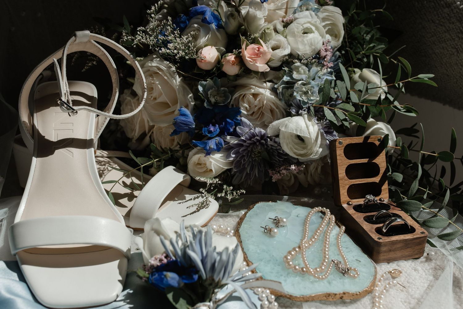 Bride's flat lay of wedding essentials with florals, heels, accessories, and ring