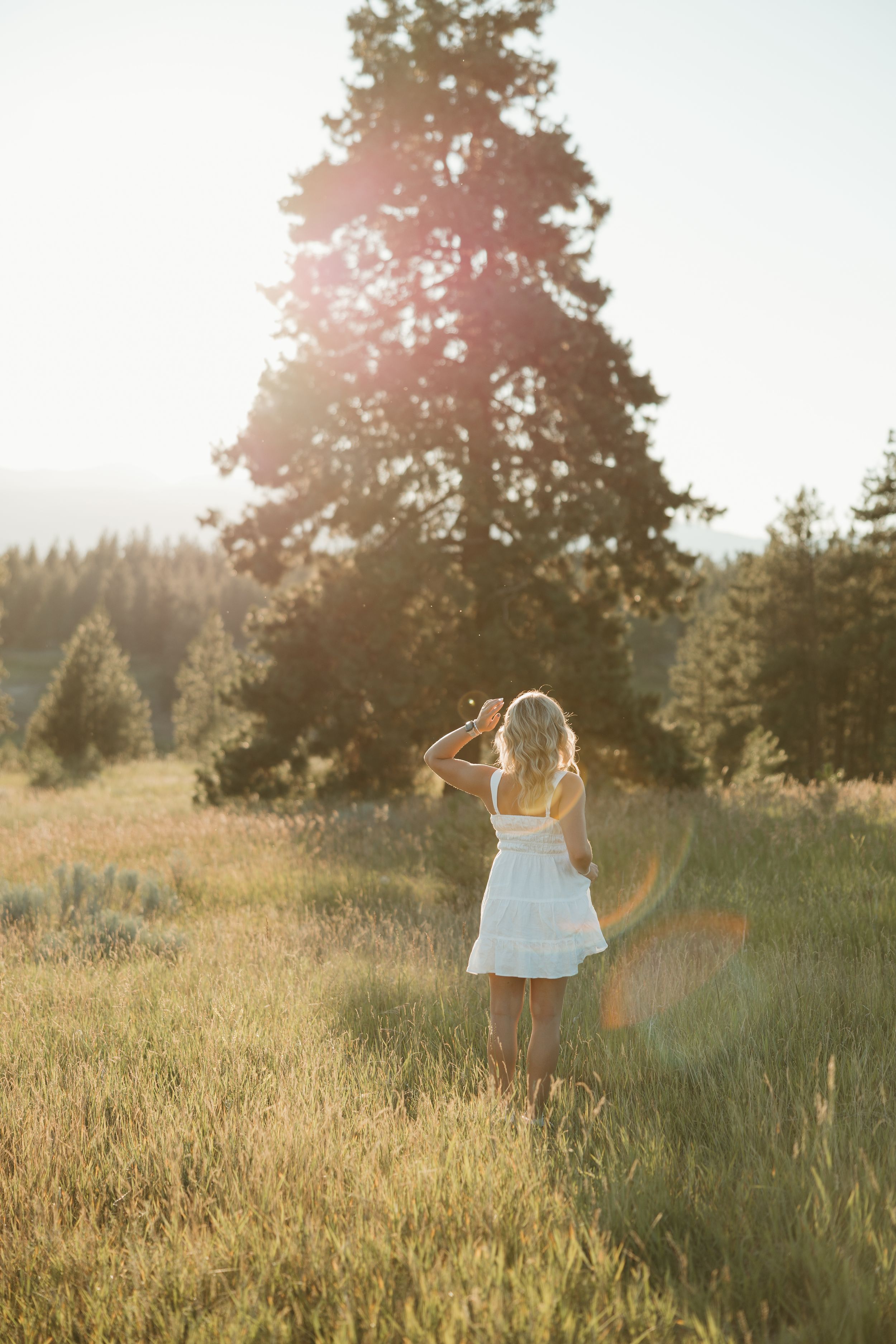 A figure in a white dress dances gracefully in a sunlit meadow during golden hour.