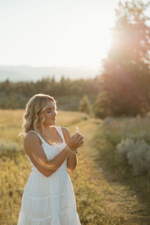 A person wearing a white dress stands in a sunlit field at golden hour in a dreamy nature setting.