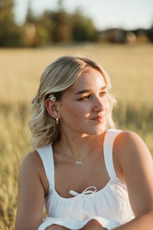 Portrait shot in golden field at sunset with white top and delicate infinity necklace.