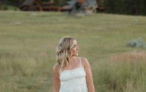 A woman in a flowing white dress walks through a sunny meadow on a summer afternoon.