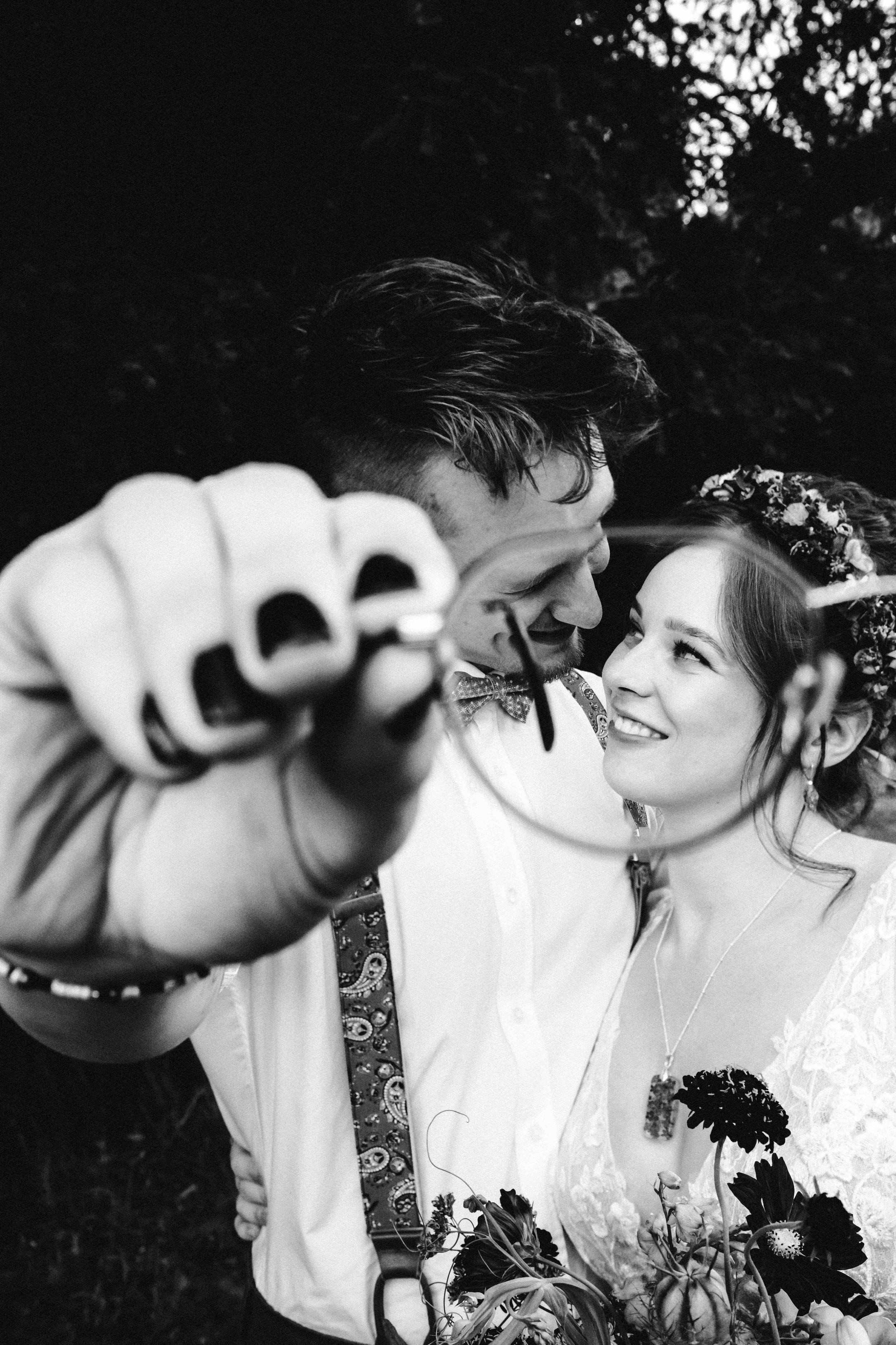 Black and white wedding photo capturing a candid laughing moment between a couple with bouquet and floral details.