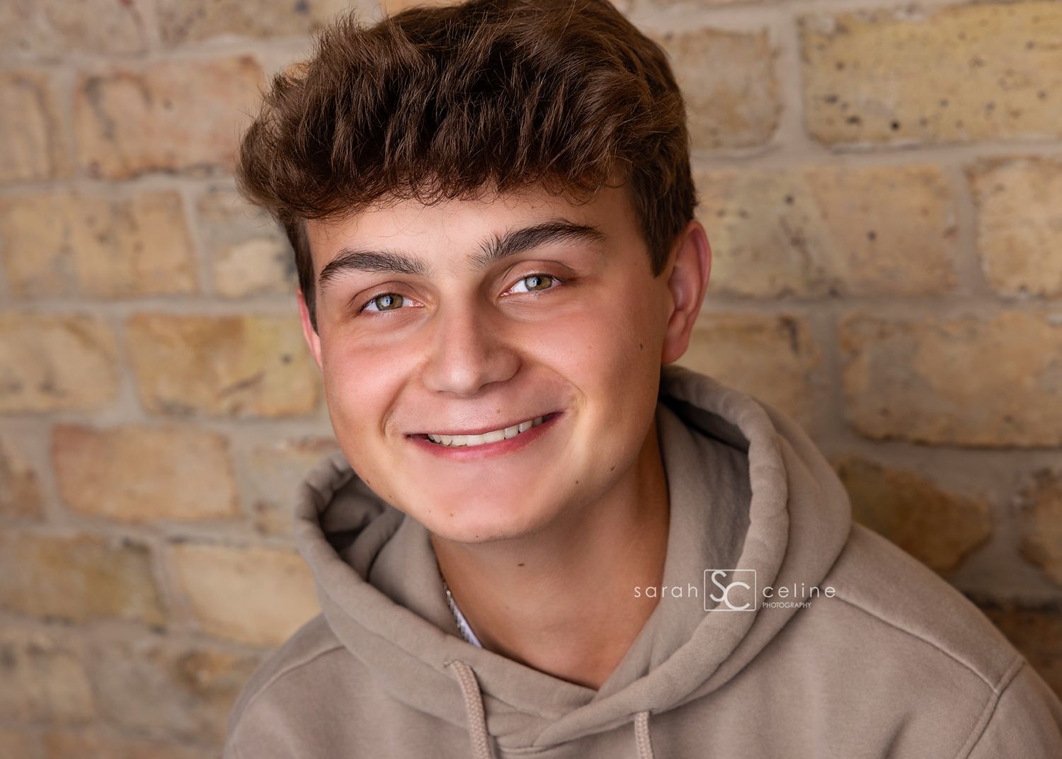 Portrait photo of someone wearing a gray hoodie against a textured stone wall background.