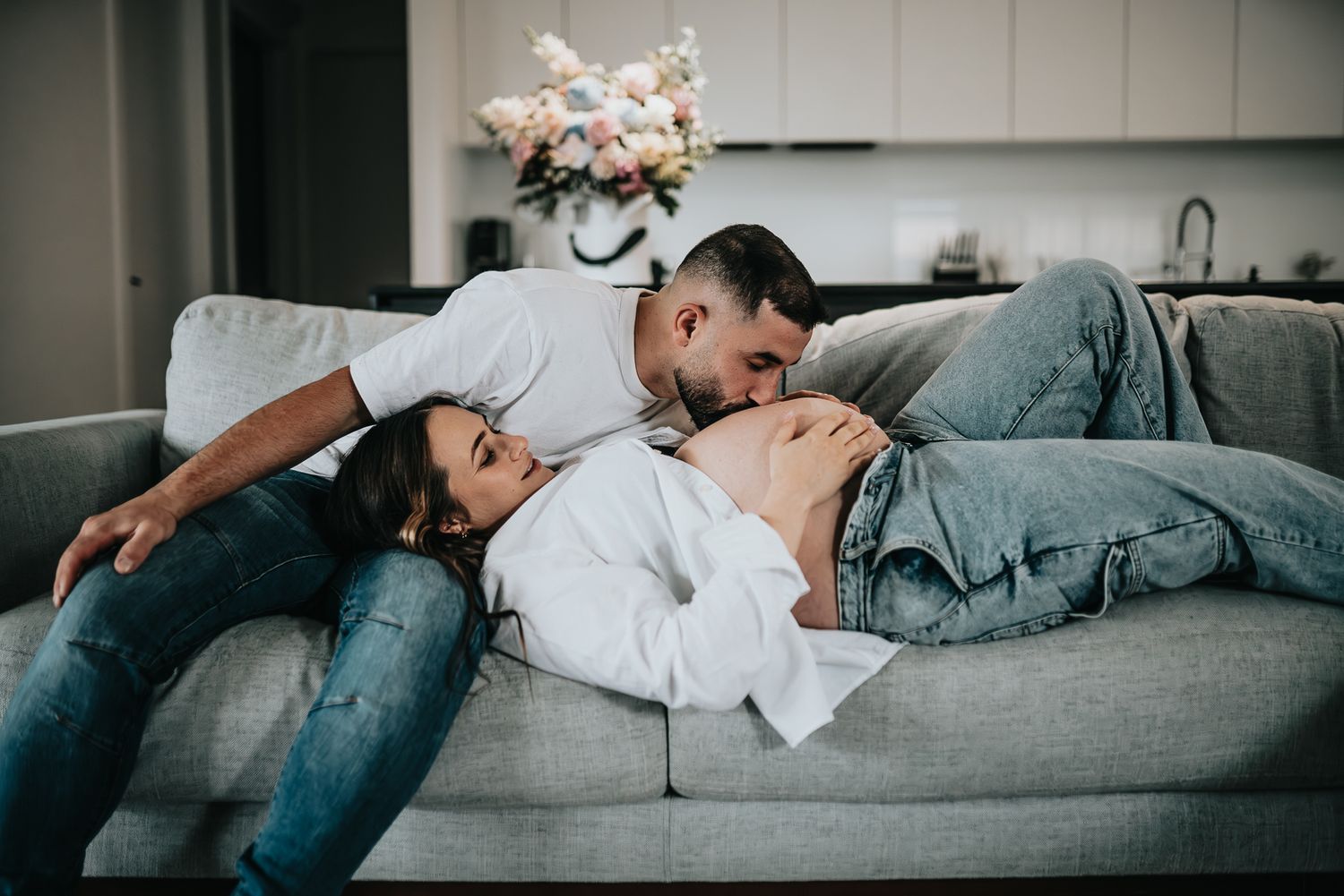 A couple in white shirts share a tender moment during a pregnancy photoshoot by bright windows by Melbourne maternity photographer.