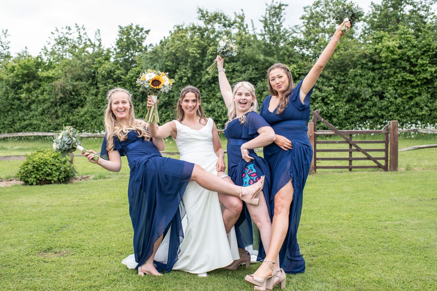 Bride and three bridesmaids in navy dresses pose and laugh for photo with bouquets in the air