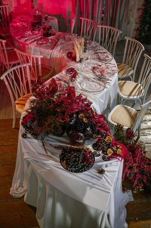 Elegant wedding reception table with white linens and dramatic red floral arrangements bathed in crimson lighting.