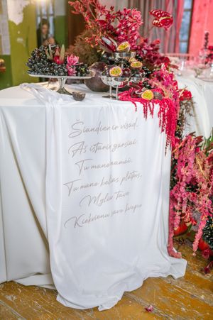 White tablecloth with elegant handwritten text sits beneath pink floral arrangements at an elegant dining table setting.