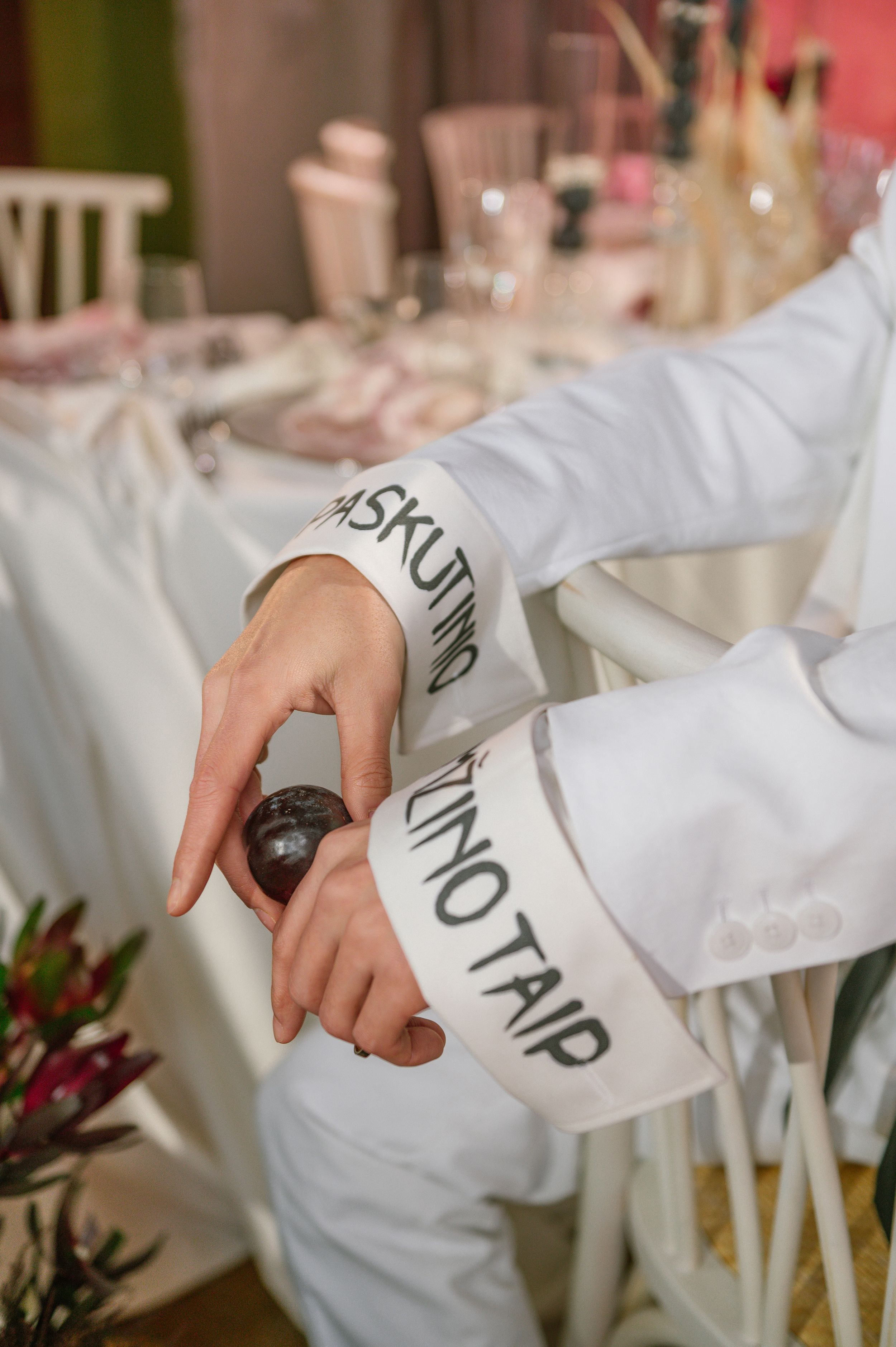 Hand wearing white sleeve with text writing reaching for something on an elegant table setting with pink decor.