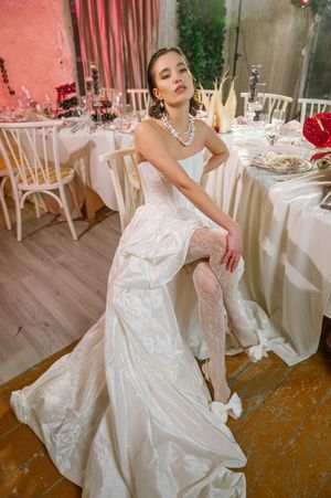 Bride in white satin wedding gown poses gracefully on wooden floor at elegant pink and white reception venue.