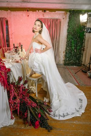 A bride in a white wedding dress poses elegantly in a pink-walled room with decorative cherry blossoms and drapery.