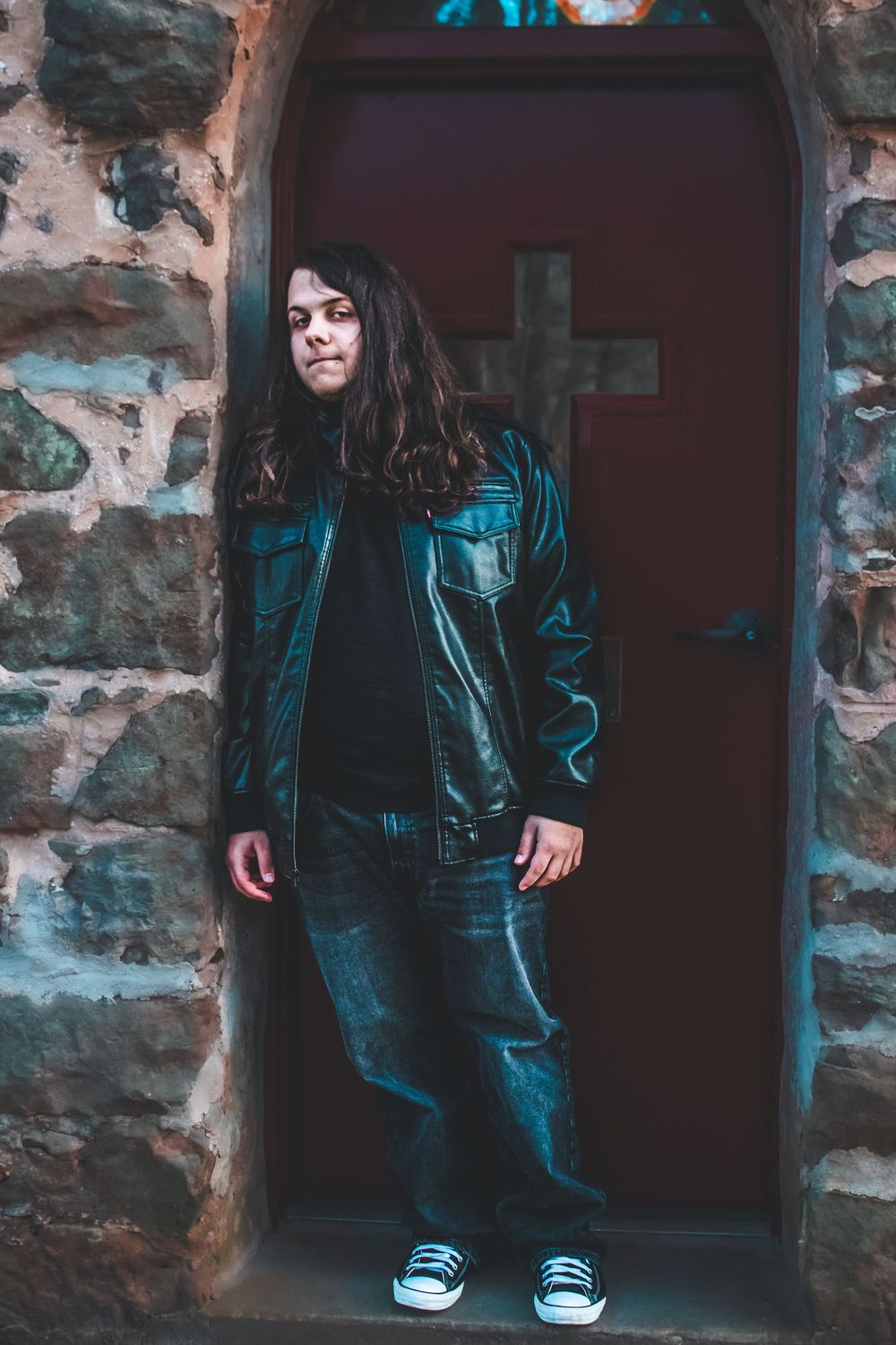 Senior boy standing in front of church door with cross on it.
