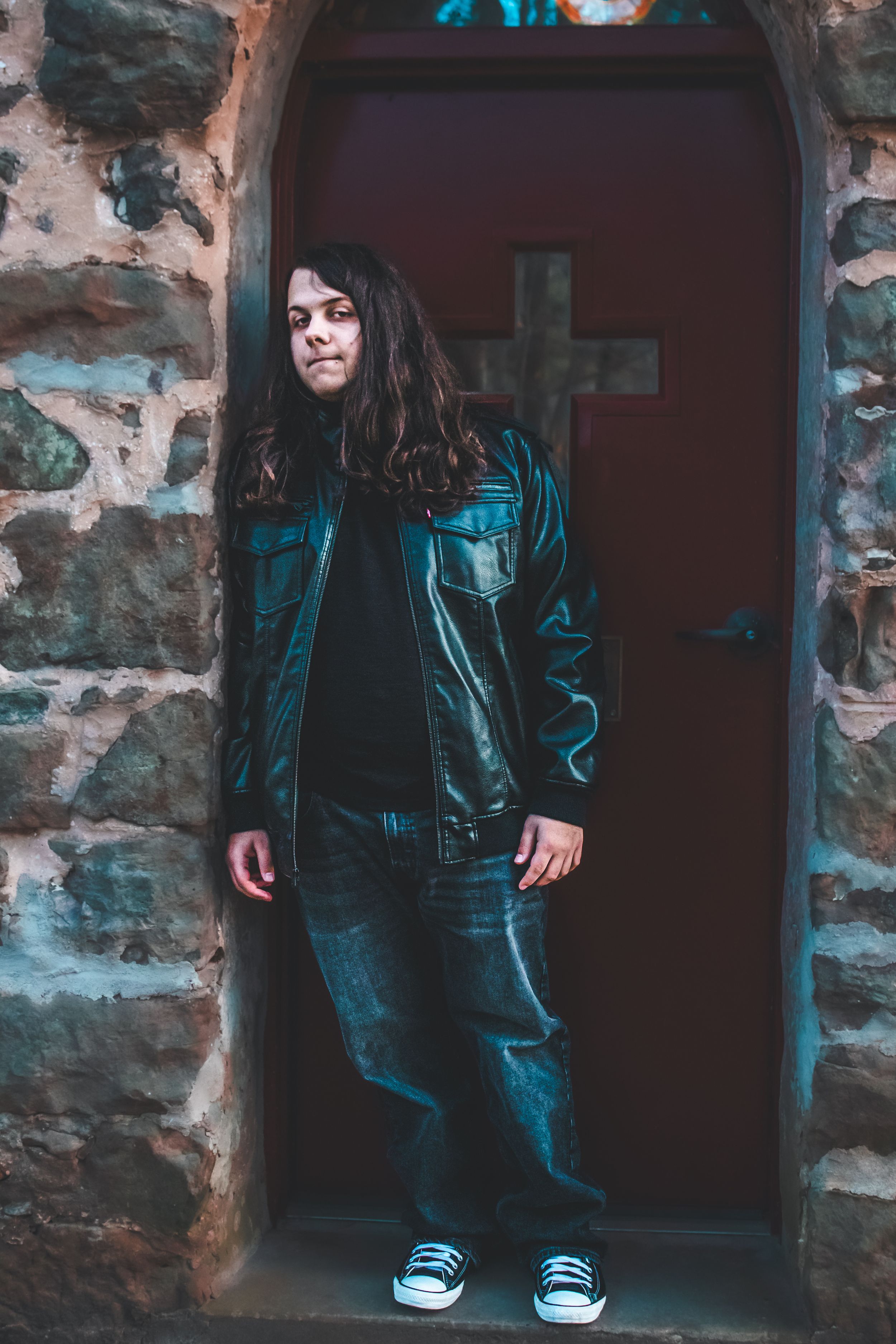 Senior boy standing in front of church door with cross on it.