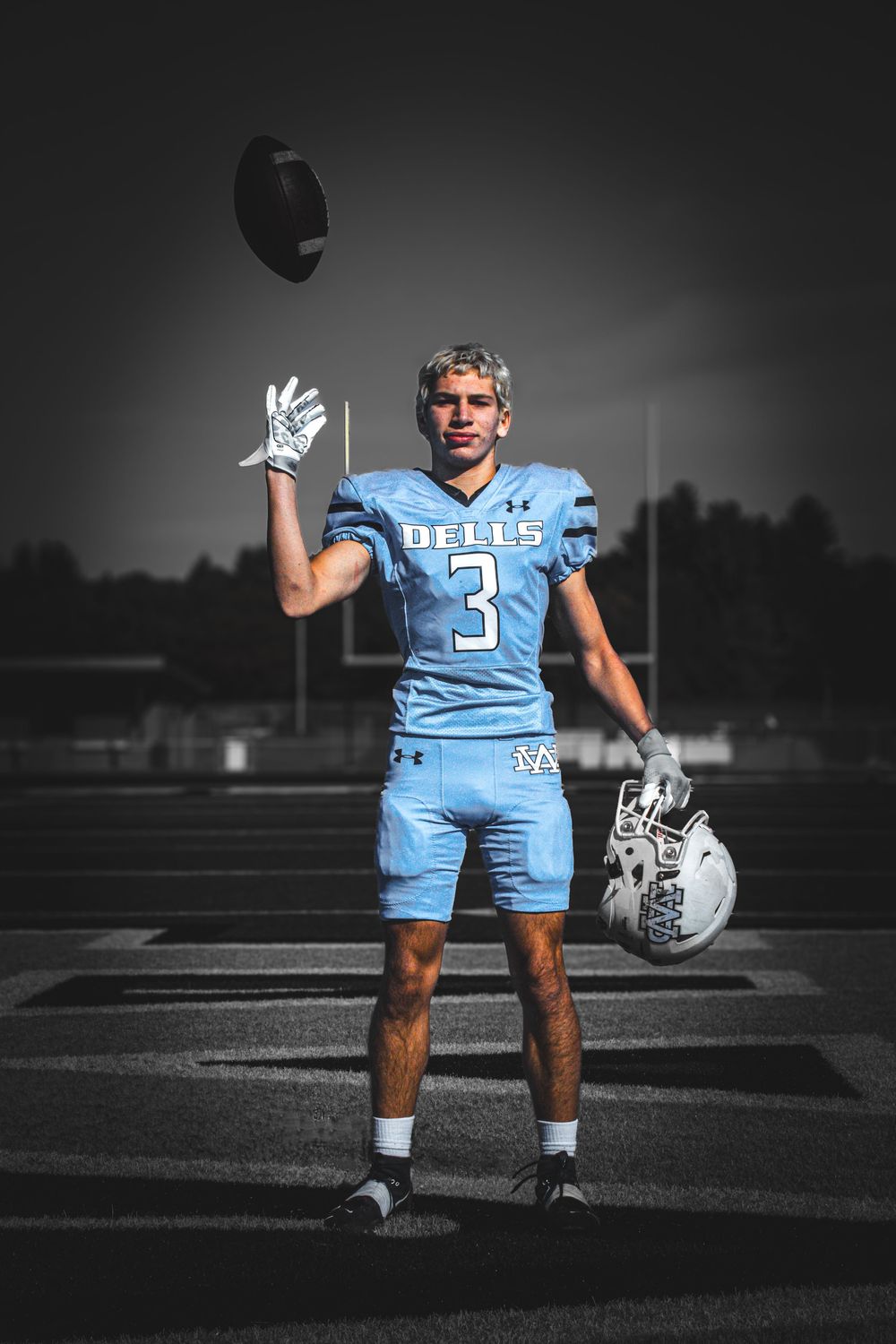 Senior boy in football uniform, on field tossing up football.