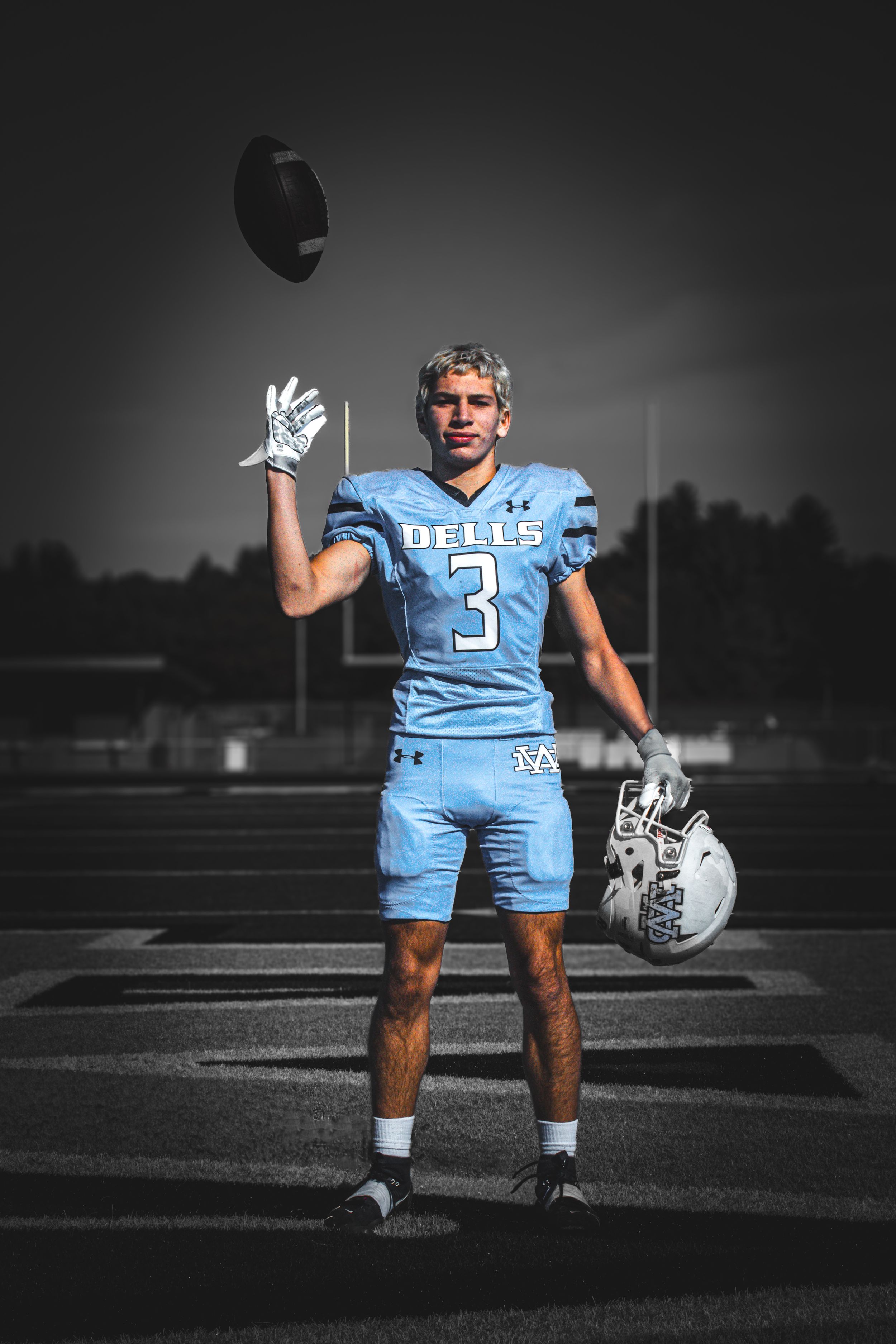 Senior boy in football uniform, on field tossing up football.