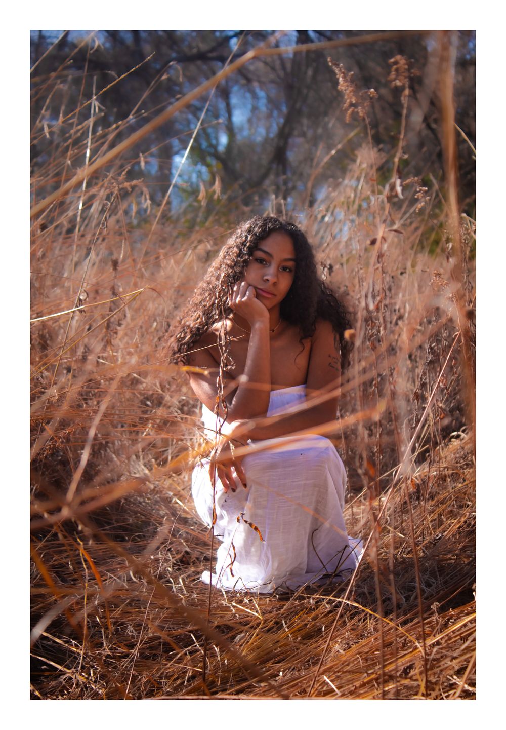 Senior girl in white dress crouching in prairie
