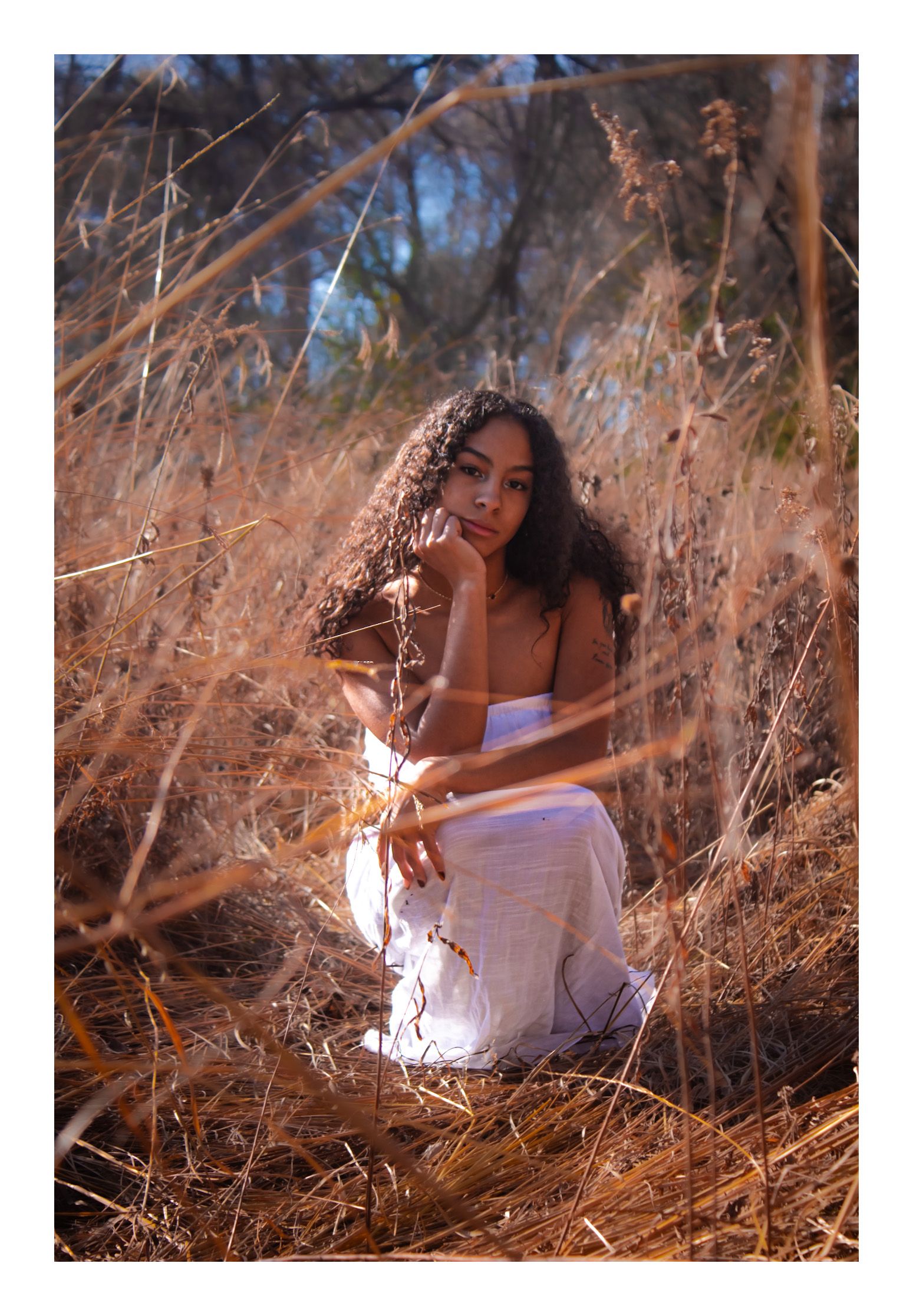 Senior girl in white dress crouching in prairie