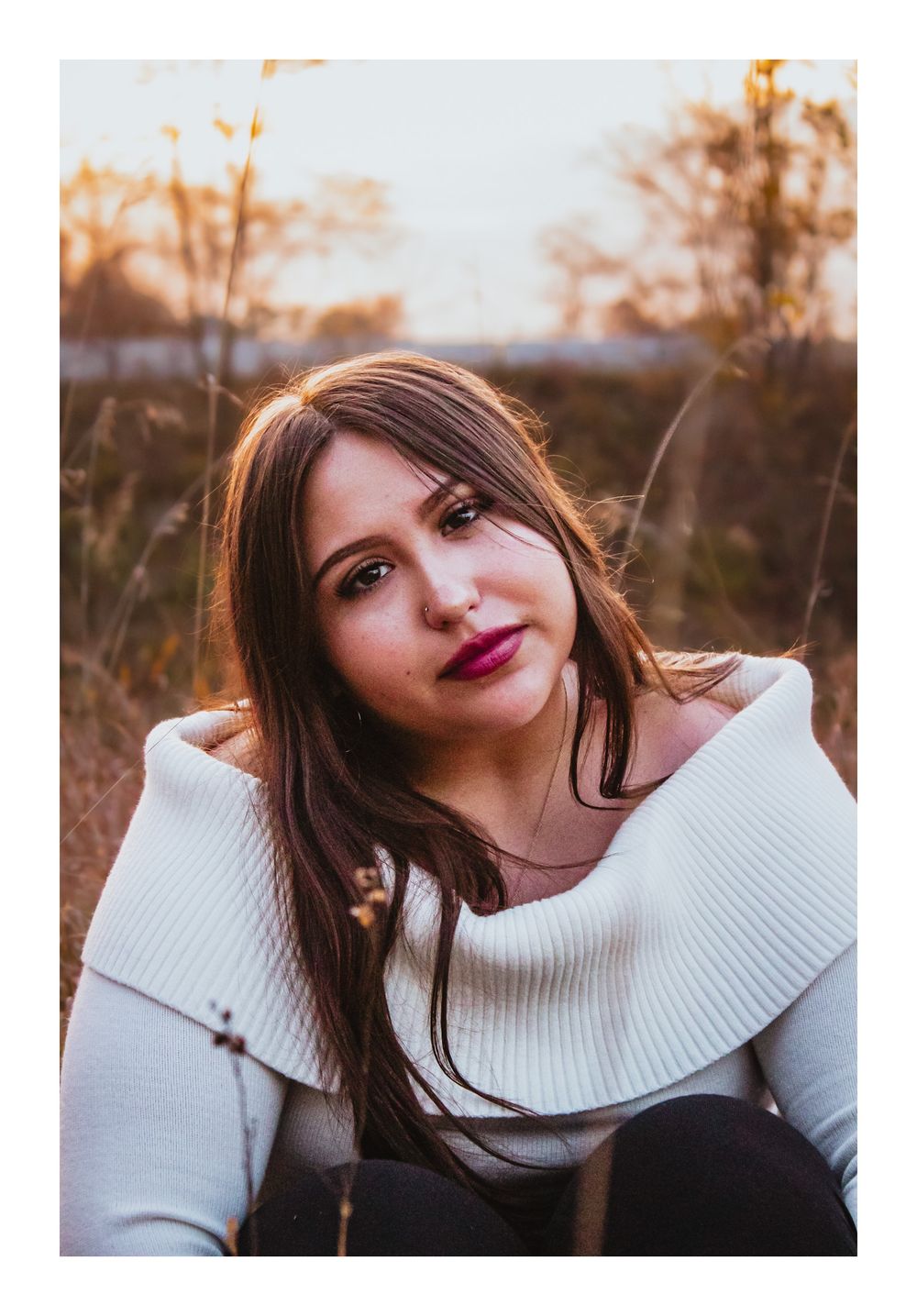 Senior girl sitting in a prairie with her headed tilted to the camera.