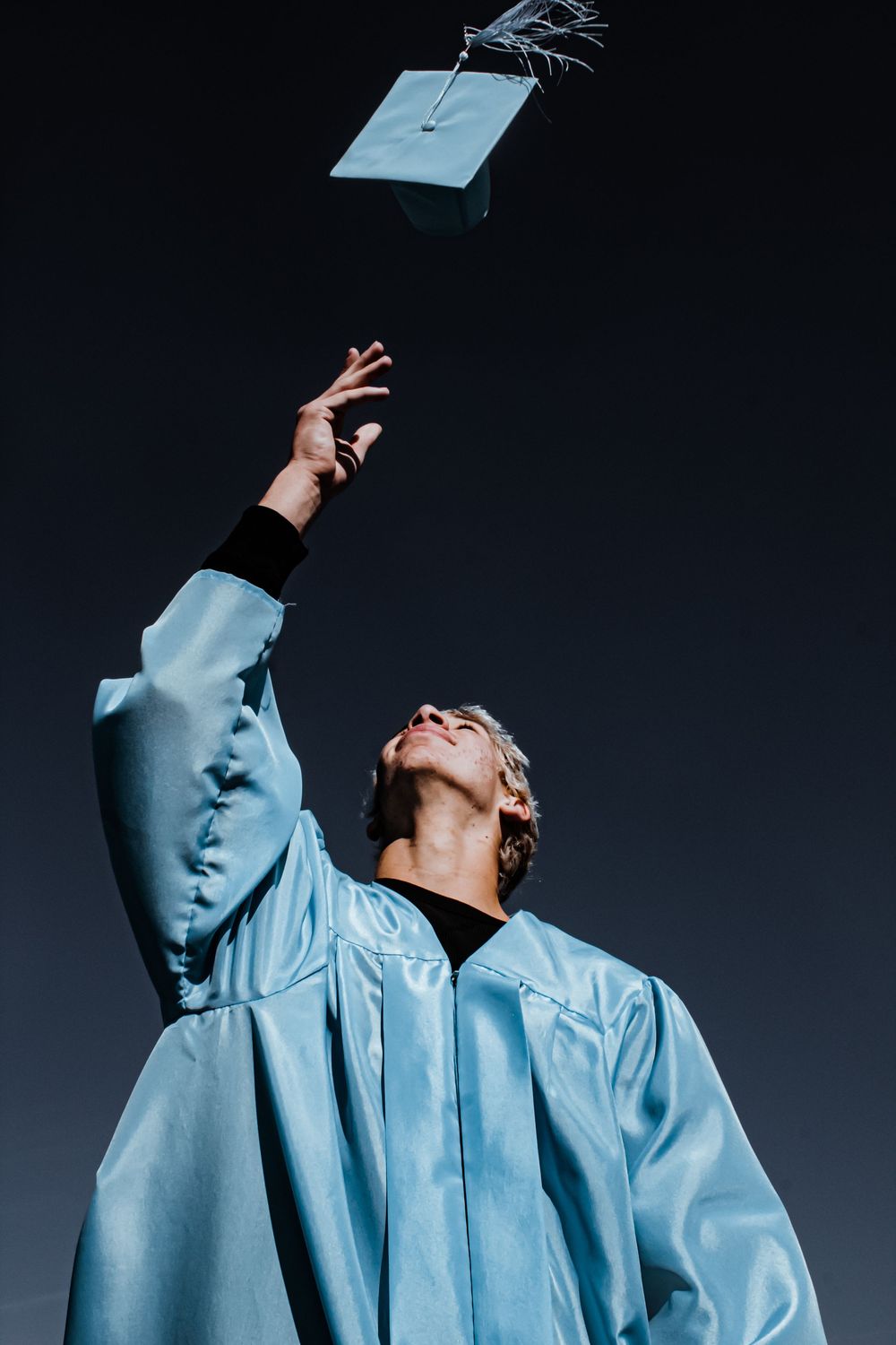 Senior boy in graduation gown, tossing up cap