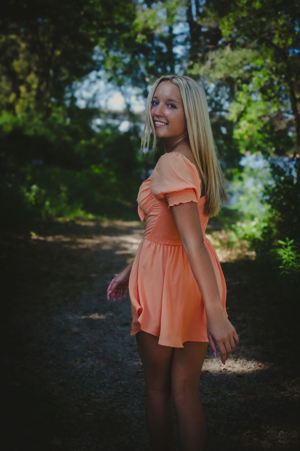 Senior girl walking down a wooded path, glancing back toward photographer.