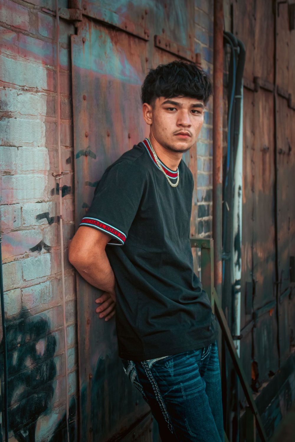 Senior boy standing with his back to an industrial wall