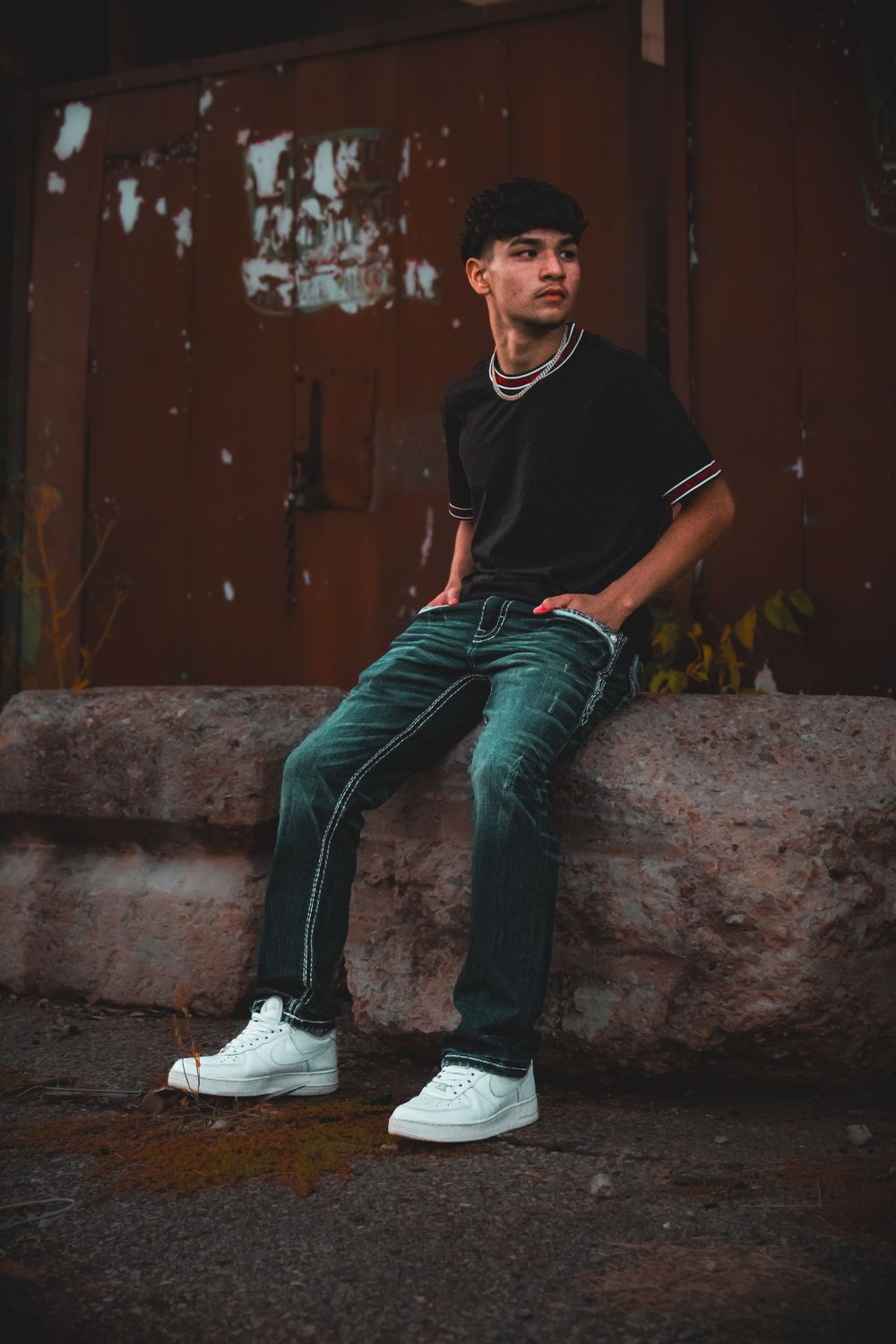 Senior boy sitting on stone wall, with hands in pocket, in front of wall with carvings