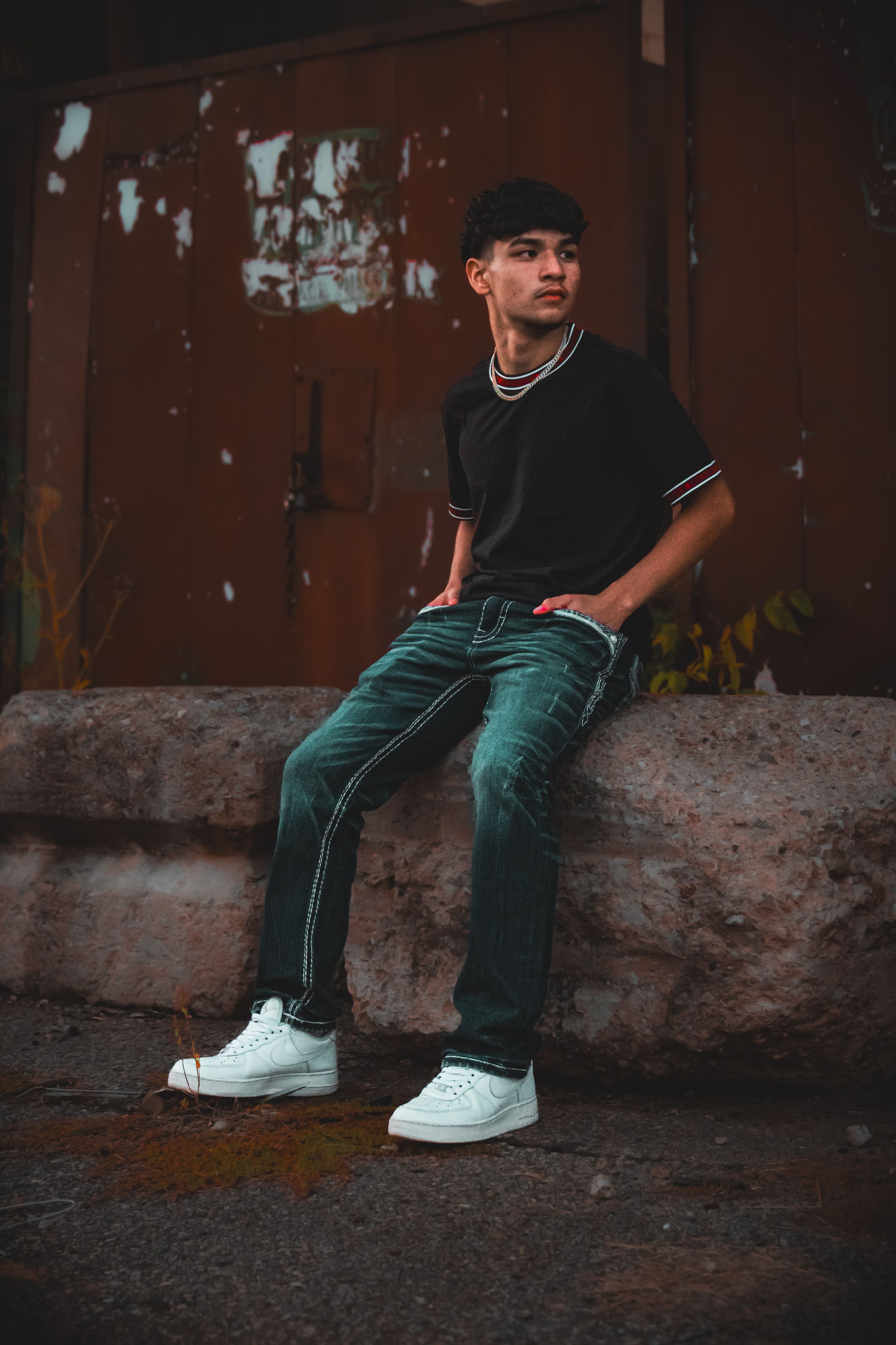 Senior boy sitting on stone wall, with hands in pocket, in front of wall with carvings