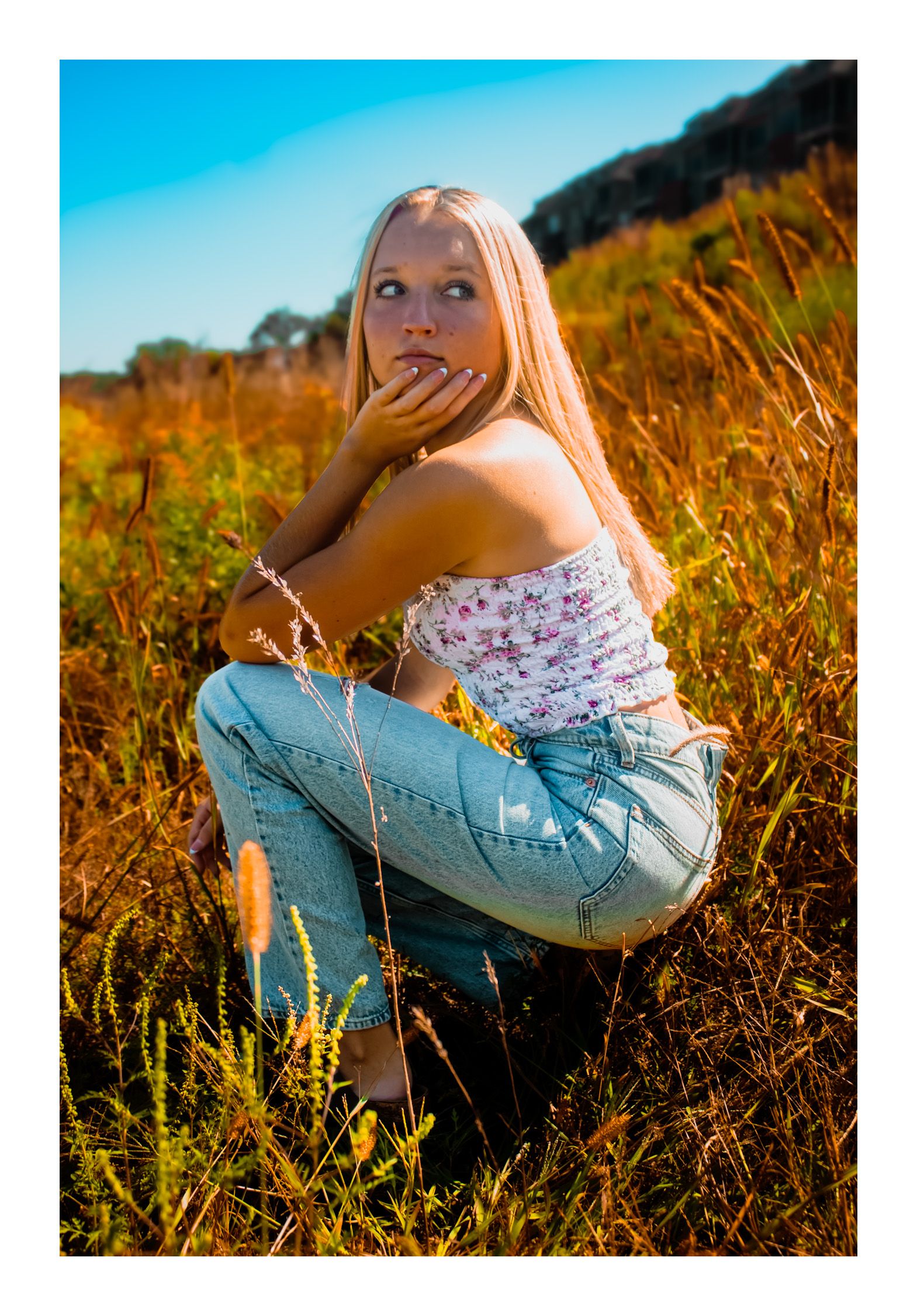 Senior girl in casual attire, crouched away from camera in a prairie