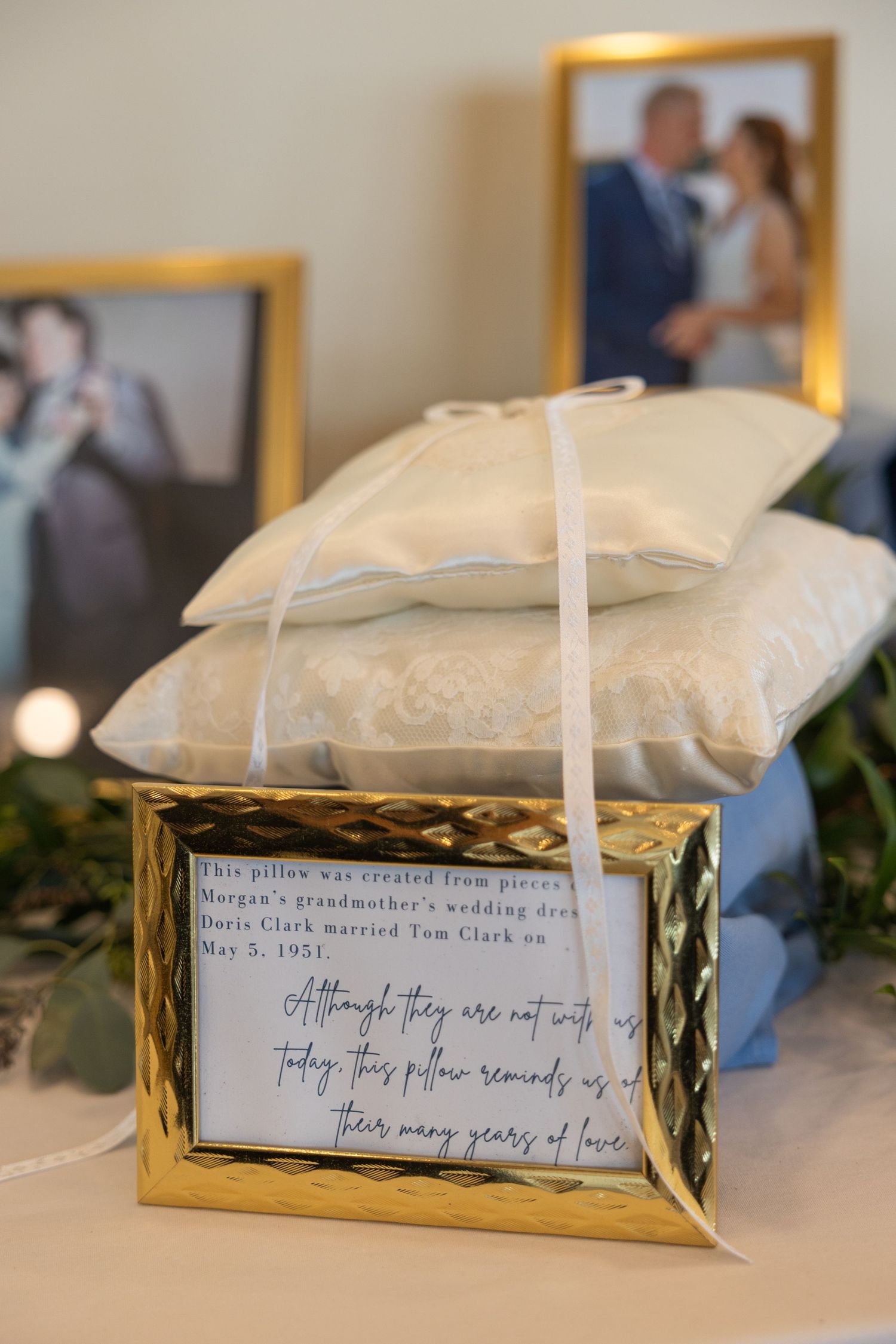 A white lace ring pillow with a handwritten family wedding heirloom note in a gold frame displayed next to wedding photos. Southeast MI