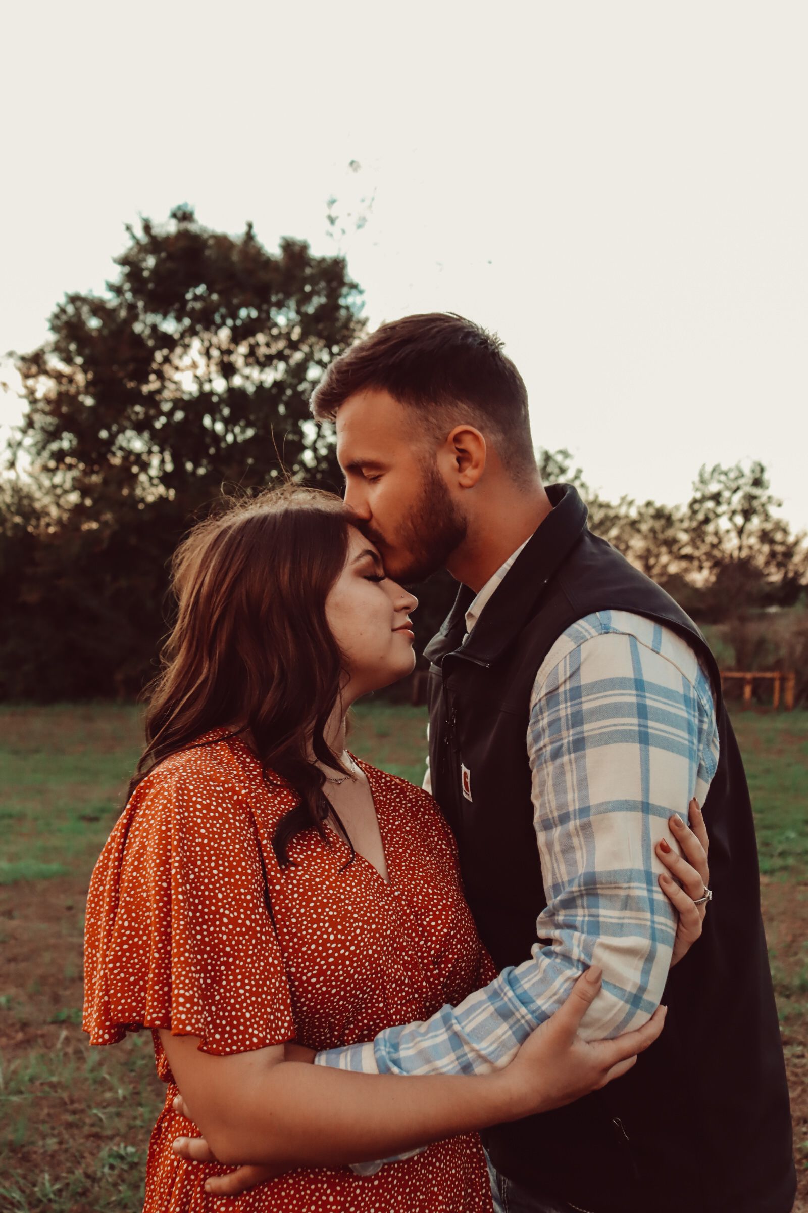 A romantic embrace at sunset with a couple wearing a plaid vest and orange polka dot dress.