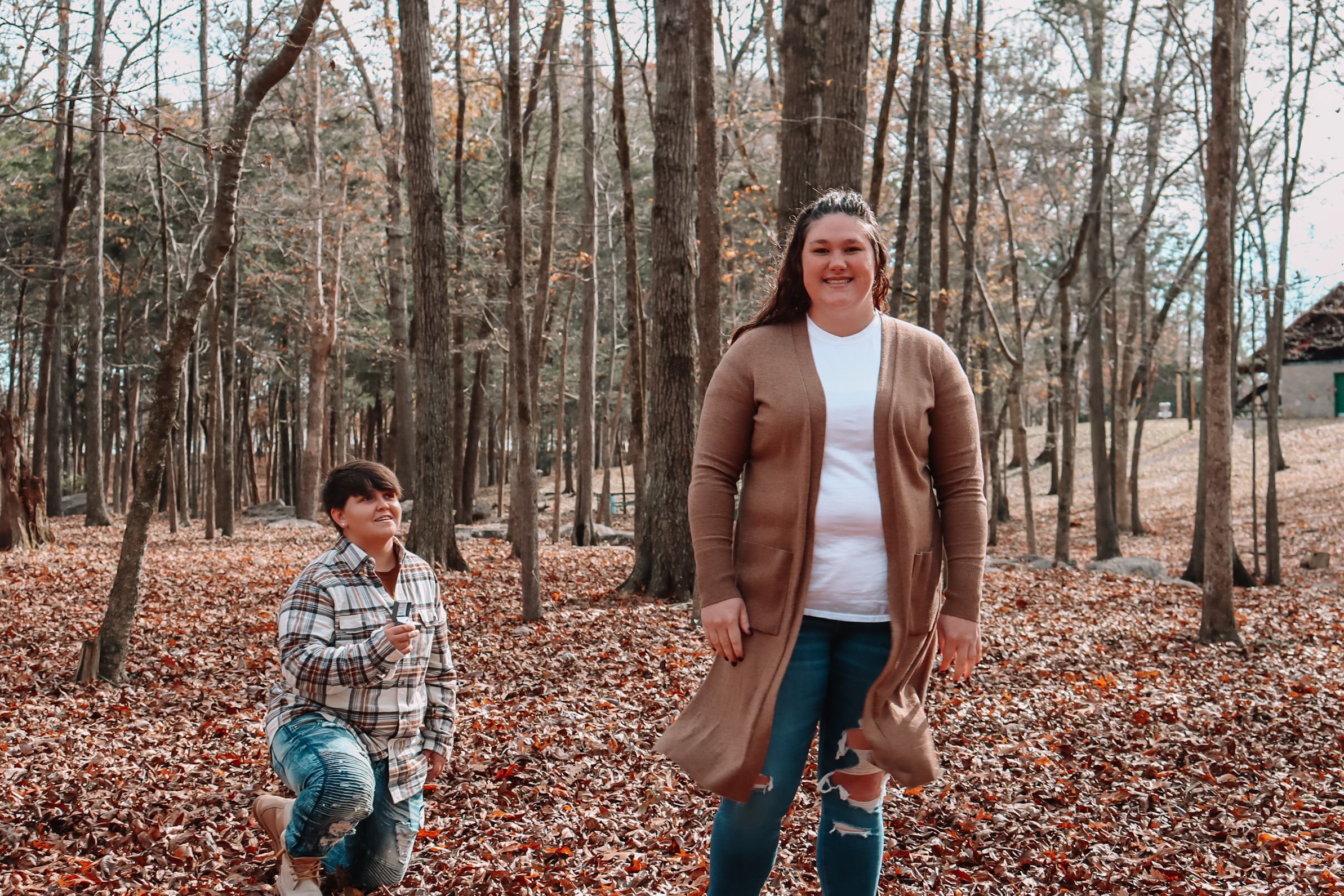 Two people walking together in a wooded area covered in autumn leaves.