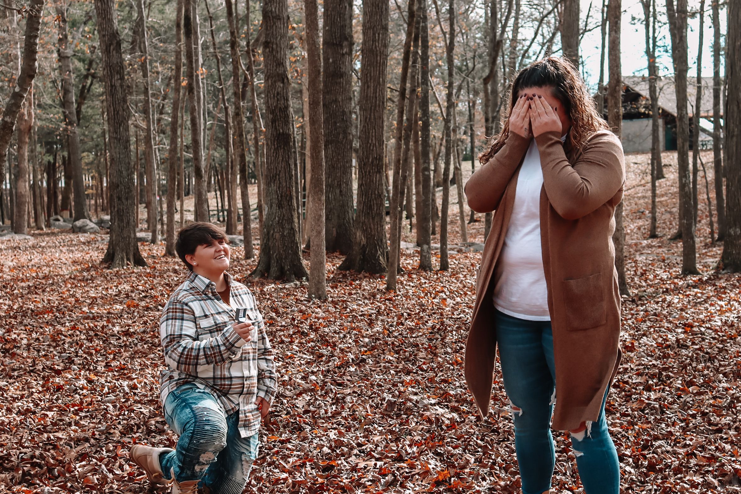 A candid moment of hide and seek being played among autumn trees with fallen leaves.