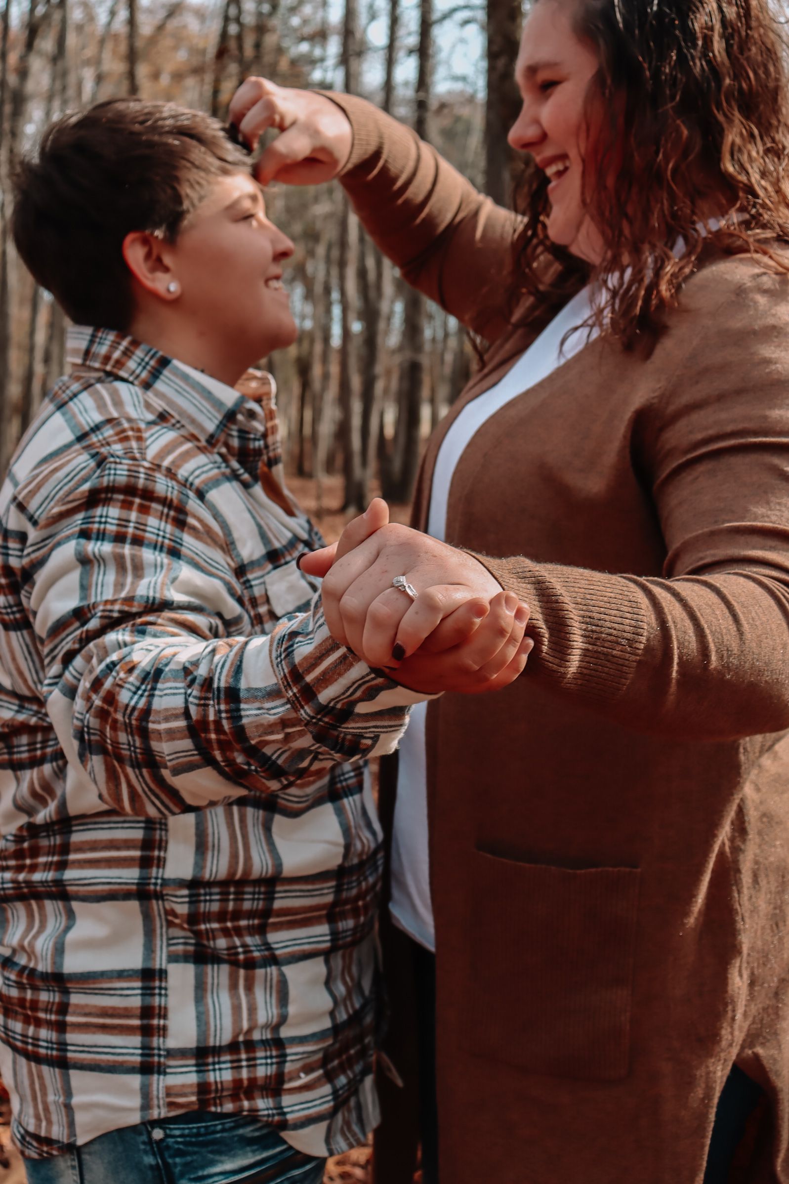 A playful moment of dancing and laughter in a forest setting wearing casual fall clothing.