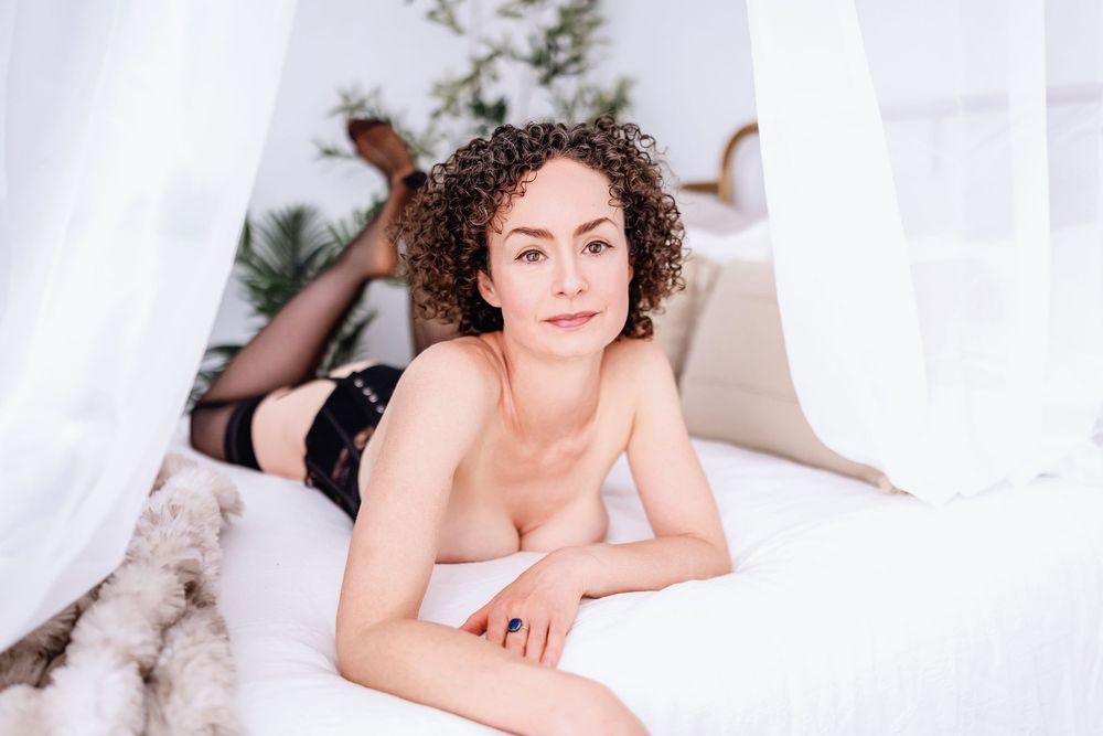 Intimate romantic boudoir photography series featuring soft natural lighting and white bedding in a bright bedroom setting.