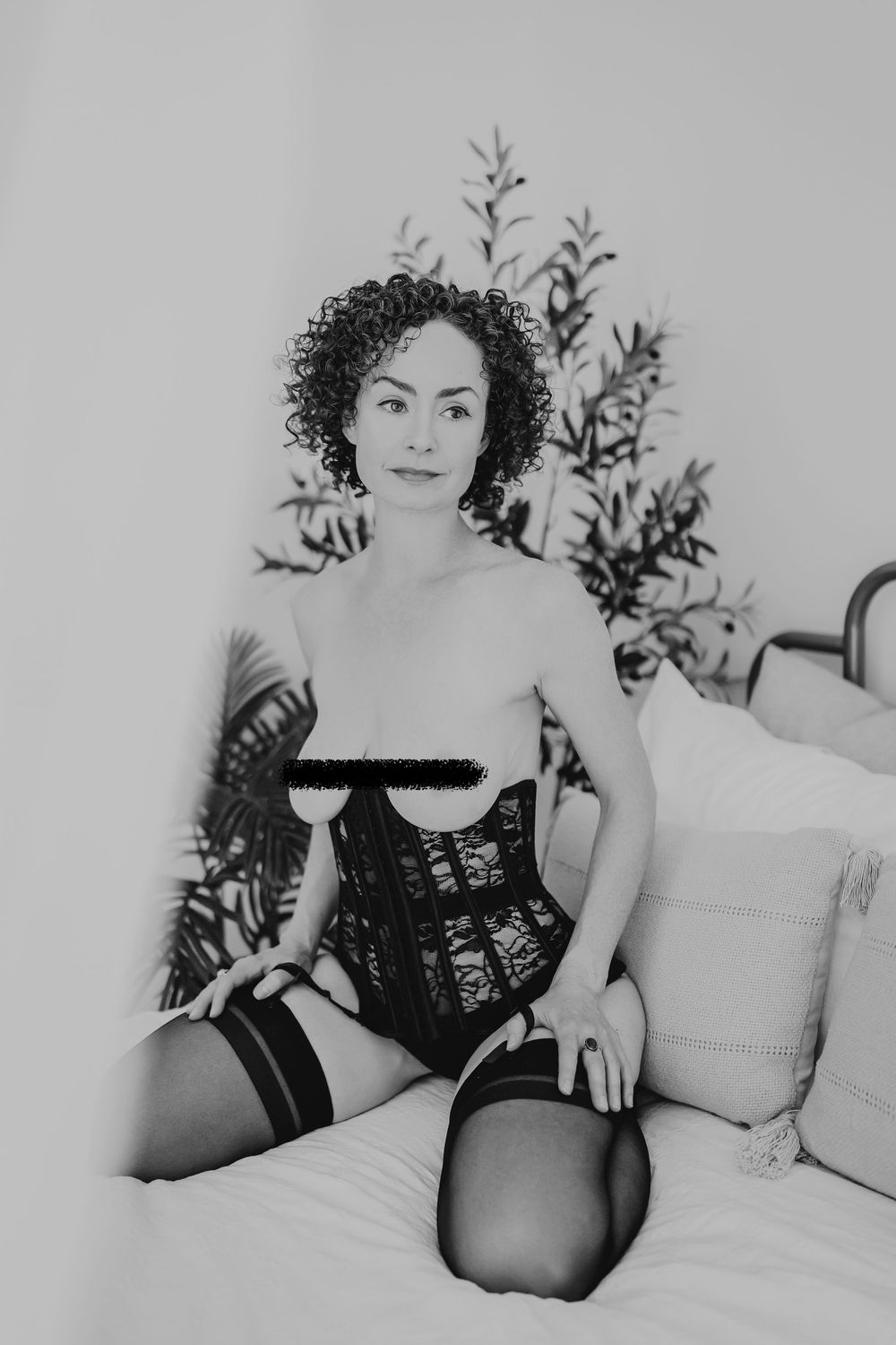 Black and white boudoir photo series featuring artistic poses on a white bed with plant elements.