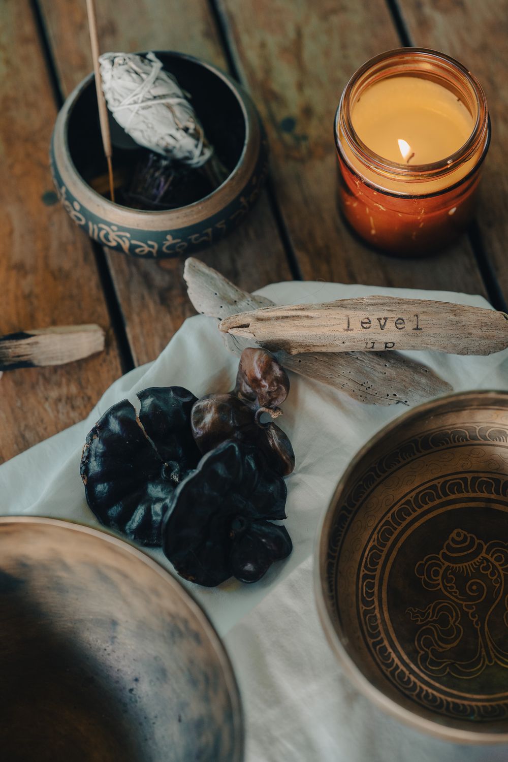 Rustic ceramic plate with ornate pattern displayed alongside purple plums and burning candle on white linen tablecloth.