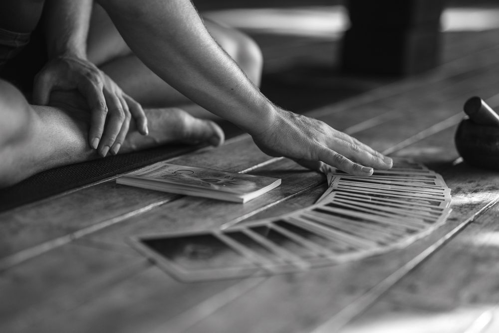 Black and white image of hands spreading out playing cards in a fan pattern on a wooden table surface.