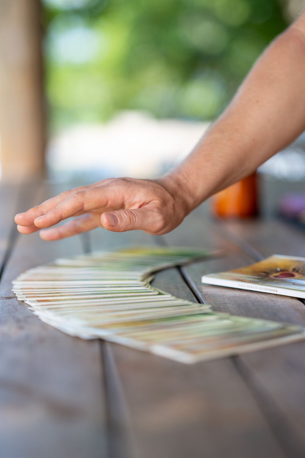 A hand hovers over a spread of cards laid out on a wooden surface with bokeh background.